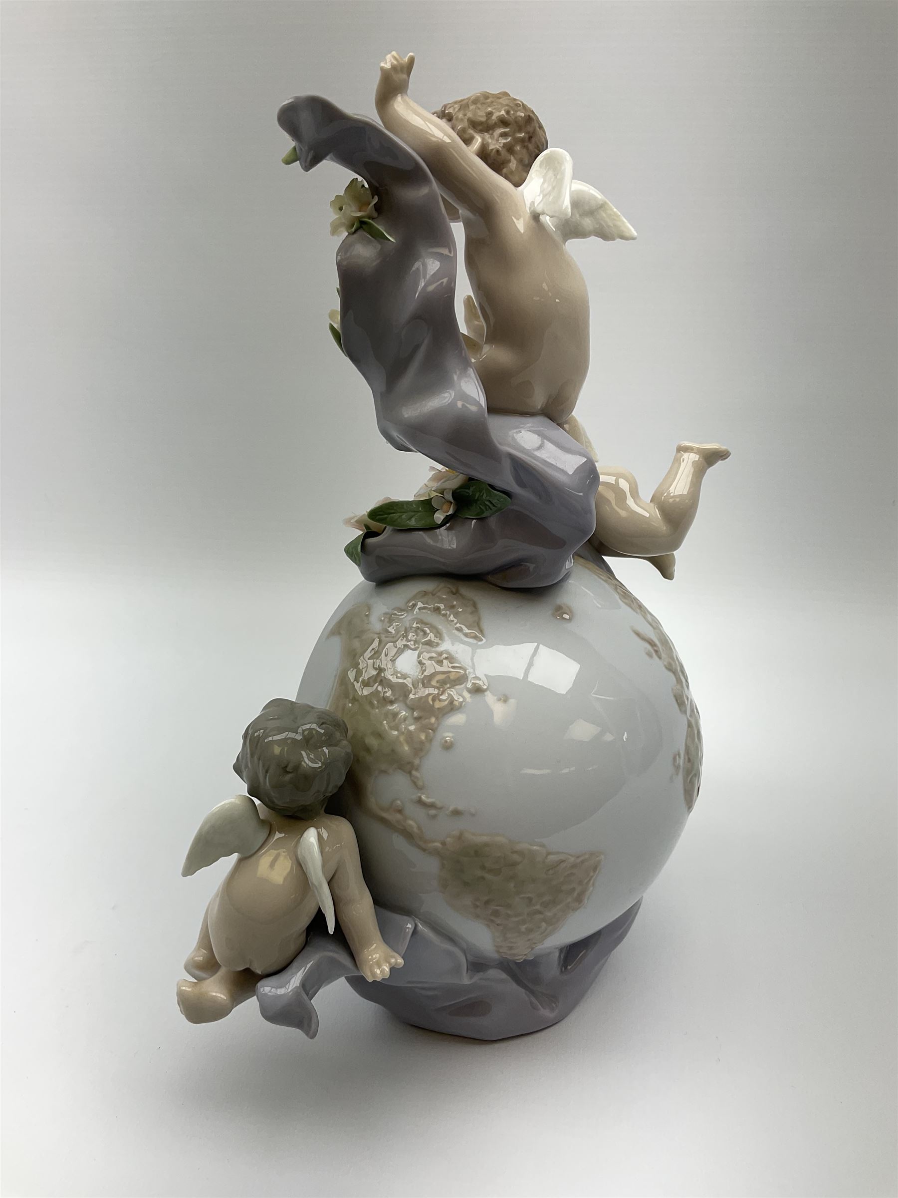 A Lladro mantel clock modelled as a globe with inset clock, surmounted by four putti and floral garlands, with blue printed mark and impressed 5973 beneath, H29cm.