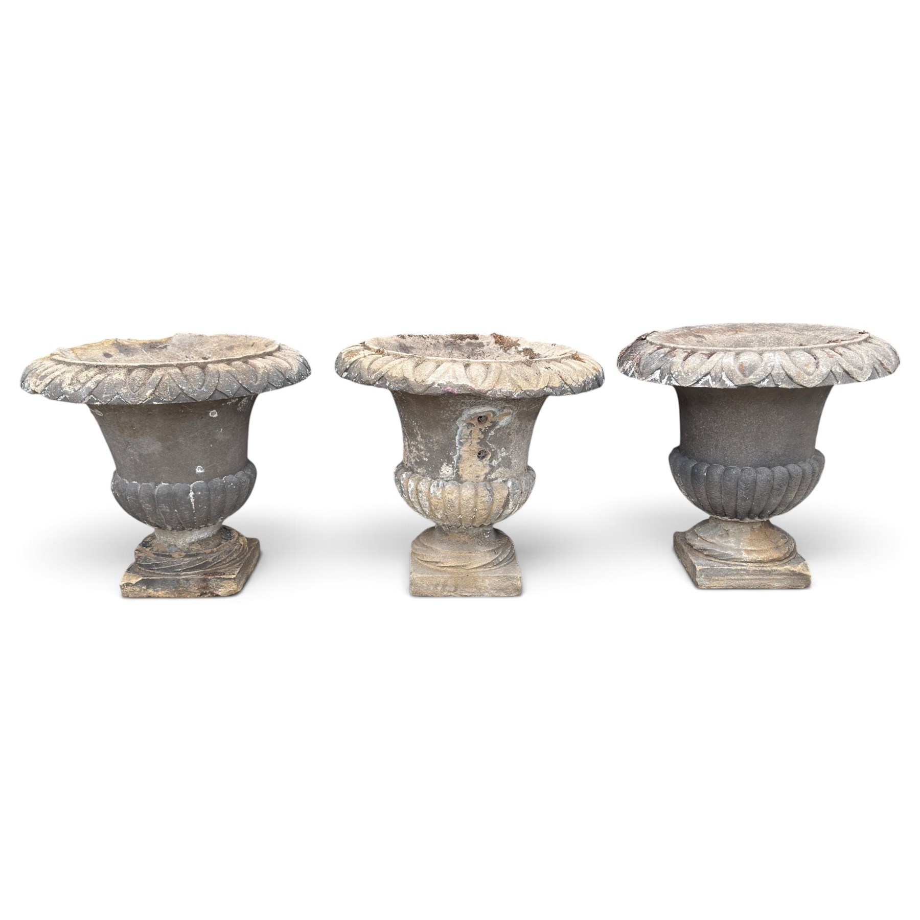 Set of three 19th century weathered carved sandstone garden urns of Neoclassical campana form, the broad everted rim carved with pointed egg-and-dart motifs, above a plain waisted bowl with gadrooned underbelly, on moulded rope-twist socle and square plinth base