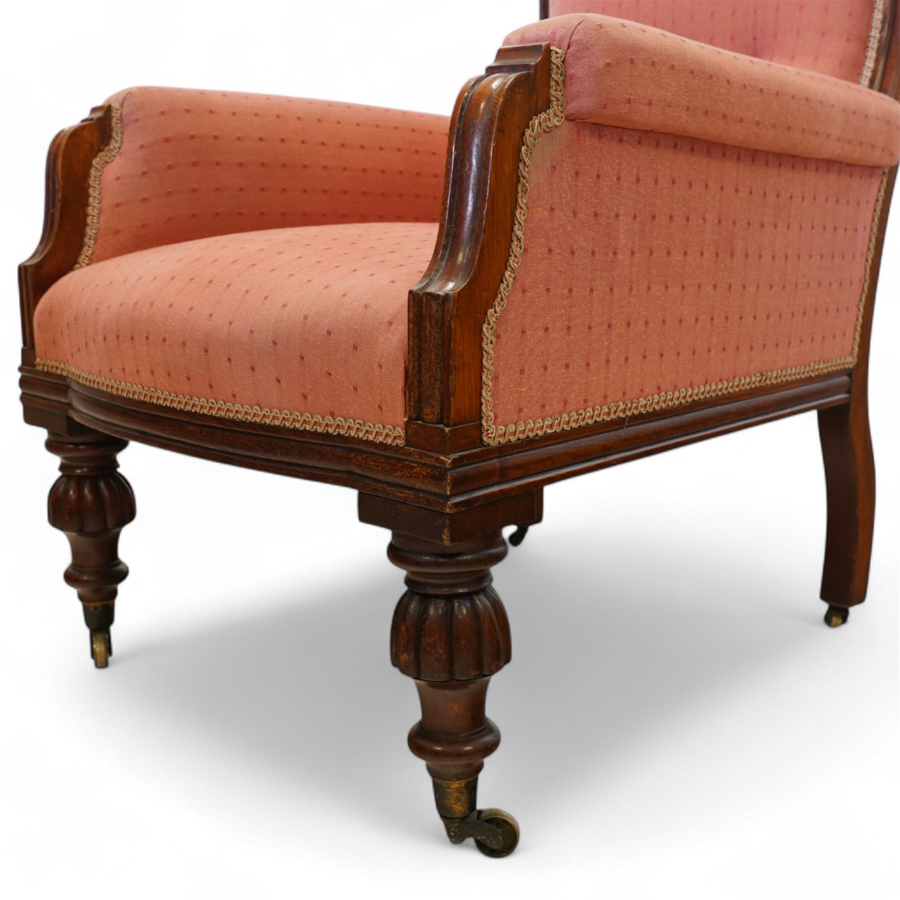 Victorian mahogany framed armchair, upholstered in salmon pink dot patterned fabric, the moulded arms with carved scroll terminals, raised on turned and fluted front legs and swept back legs, all with castors