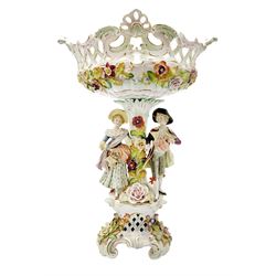 Early 20th century Sitzendorf table centrepiece, modelled as a floral encrusted column flanked by male and female figures, he with watering can, she with basket of flowers, supporting a scrolling, part pierced and floral encrusted basket with hand painted floral sprays to the interior, the whole upon a conforming base, with blue hatched mark beneath, H50cm, basket L36cm