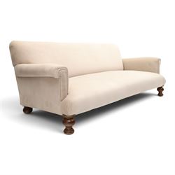 Late Victorian oak framed low three-seat settee, of traditional shape with low rolled sprung back over rolled arms and sprung seat, raised on front turned feet, upholstered in beige fabric