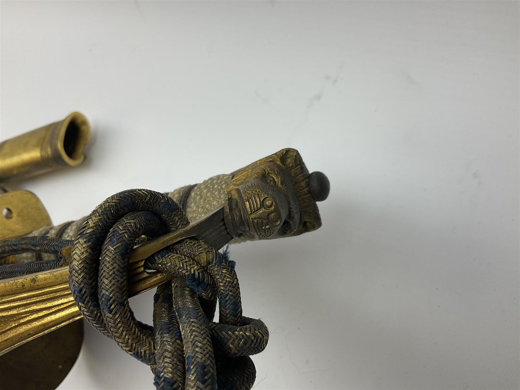 WW1 George V era 1827 Pattern Royal Naval Officer’s sword, the 80cm fullered steel blade decorated with crown, fouled anchor etc and marked Gieves Portsmouth London Edinburgh Devonport to the ricasso, gilded hilt with fouled anchor and crown, wire-bound ray skin grip, lion’s head pommel with mane backstrap, folding/locking langet and full bullion knot; in  leather scabbard having twin brass lockets with hand engraved panels and twin suspension rings L94cm overall. Provenance: By direct family descent from Brian Heathcote HMS Conqueror later Superintendant in the Liverpool Special Constabulary.