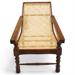 20th century teak framed plantation chair, plain cresting rail over cane back and seat, fitted with hinged extending leg rests, raised on turned front-supports united by ring-turned stretcher