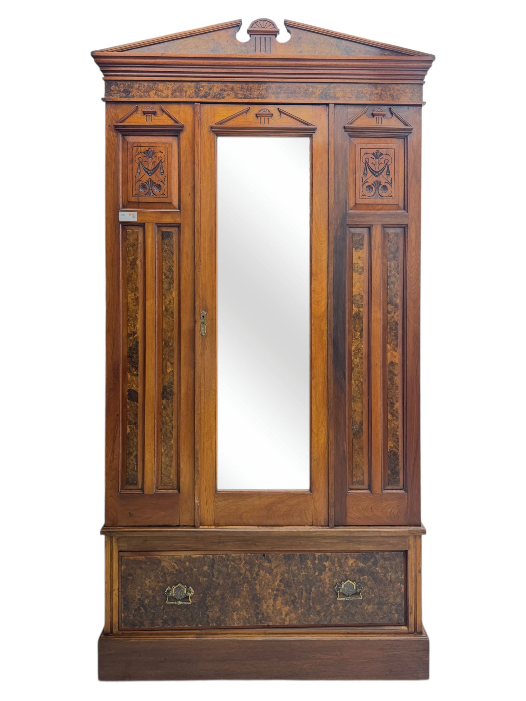 Victorian walnut bedroom suite - wardrobe, dressing chest and bedside cupboard, comprising a full-length wardrobe with broken pediment and central mirrored door, large lower drawer, a matching dressing table with bevelled swing mirror over two trinket drawers and two short drawers over two long drawers, and a single-door bedside cupboard, all with moulded edges, decorative panel work and shaped aprons