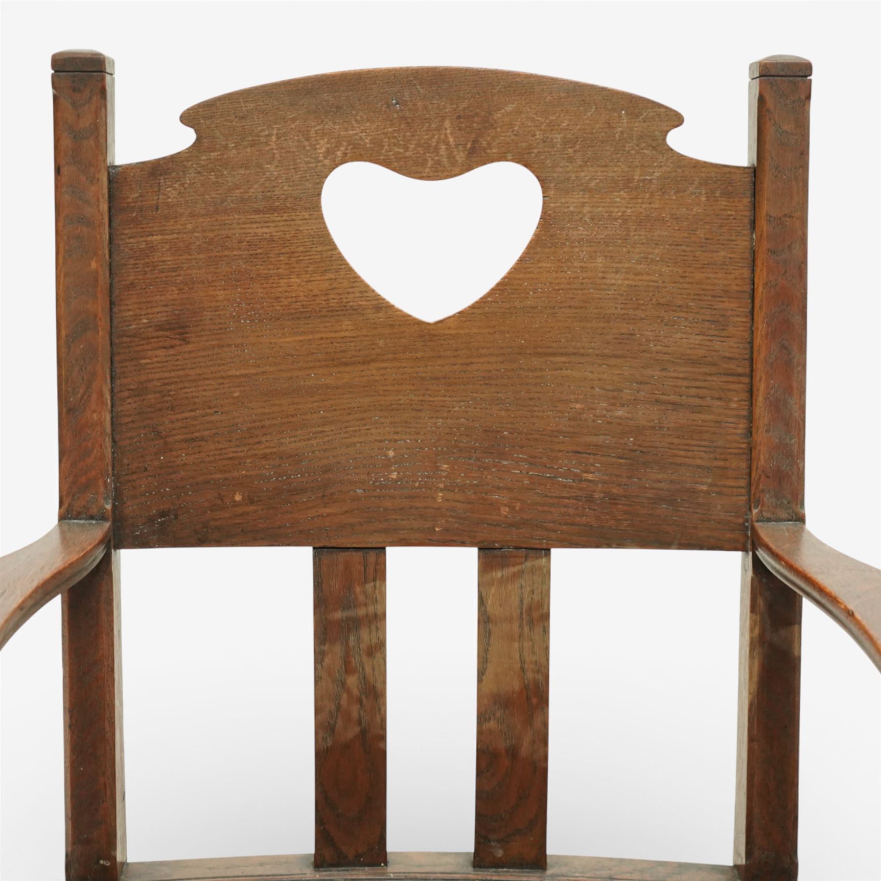 Arts and Crafts oak armchair, the shaped back with heart-shaped pierced splat above three vertical slats, solid dished seat with rounded front, open arms on turned front supports, square section legs united by plain stretchers