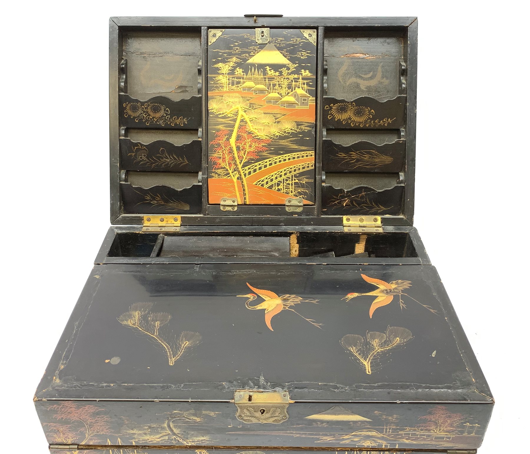  A 20th century Chinese black lacquer and gilt detailed writing box, decorated with figures, pagodas and cranes amidst a mountainous landscape, the hinged cover opening to reveal a compartmented interior and fold out baize lined slope, H20cm L46.5cm D31.5cm.   