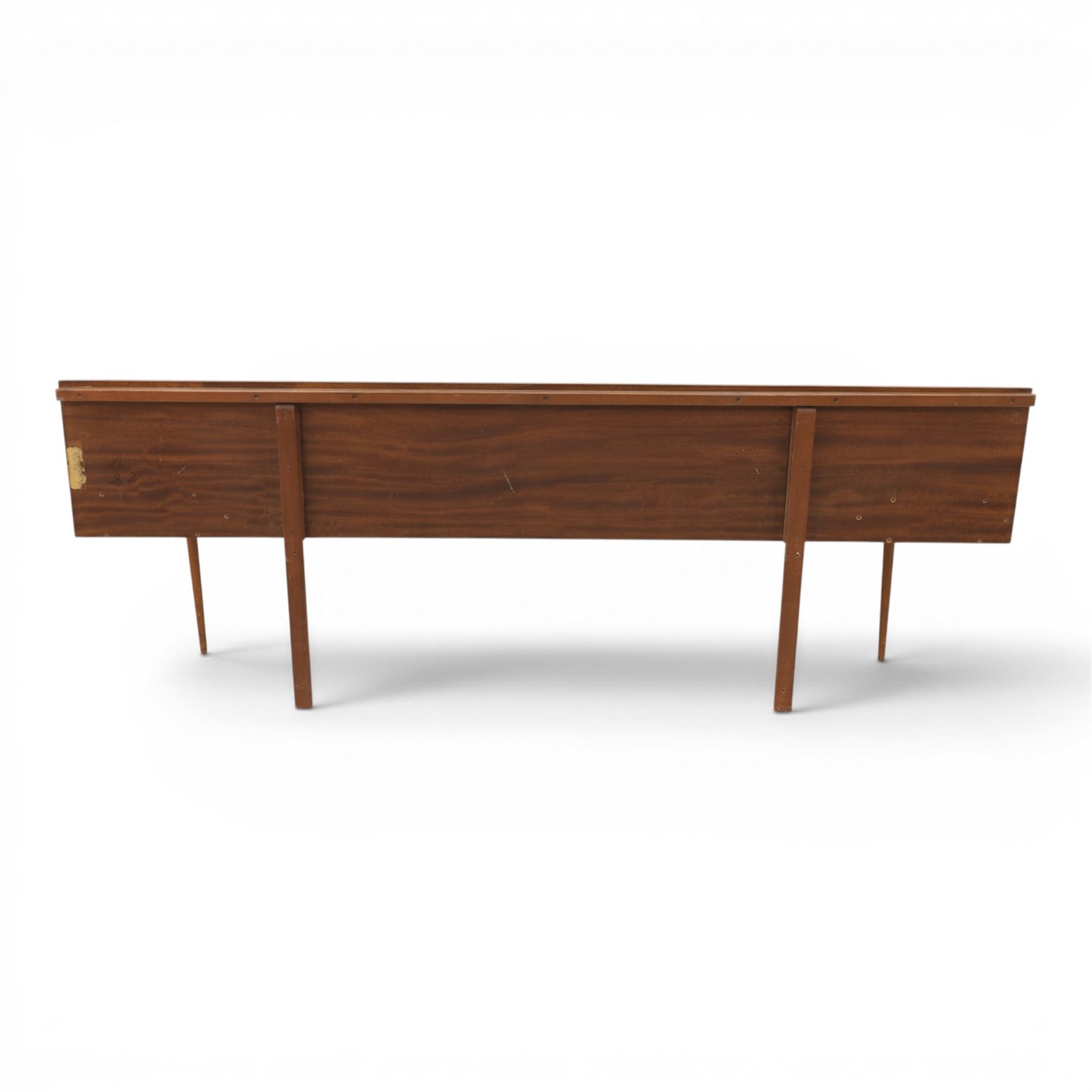 Austinsuite - mid 20th century teak headboard with bedside cabinets and matching  mirrored dressing table, the headboard with floating single drawer bedsides raised on a single tapering support, the dressing table with attached tilting mirror, above rectangular top with kneehole and two banks of two drawers, raised on tapering supports

Headboard H 84cm, D 40cm, W 229cm, W between bedsides 151cm 
Dressing table H 113cm D 44cm, W 149cm, H to underside of dresser 61cm