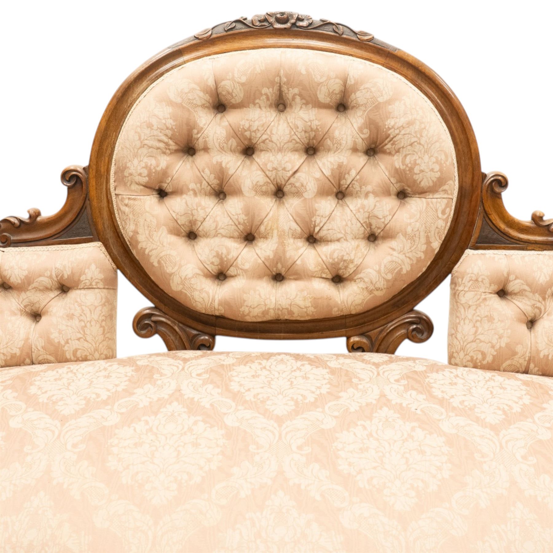 Victorian carved walnut framed double-ended settee with serpentine front, the central oval cameo back with flowerhead carved cresting rail, flanked by foliate C-scroll spandrels, the scroll carved arm terminals over floral carved cabriole supports with scroll feet and ceramic castors, the buttoned back and sprung seat upholstered in pale pink foliate patterned damask fabric