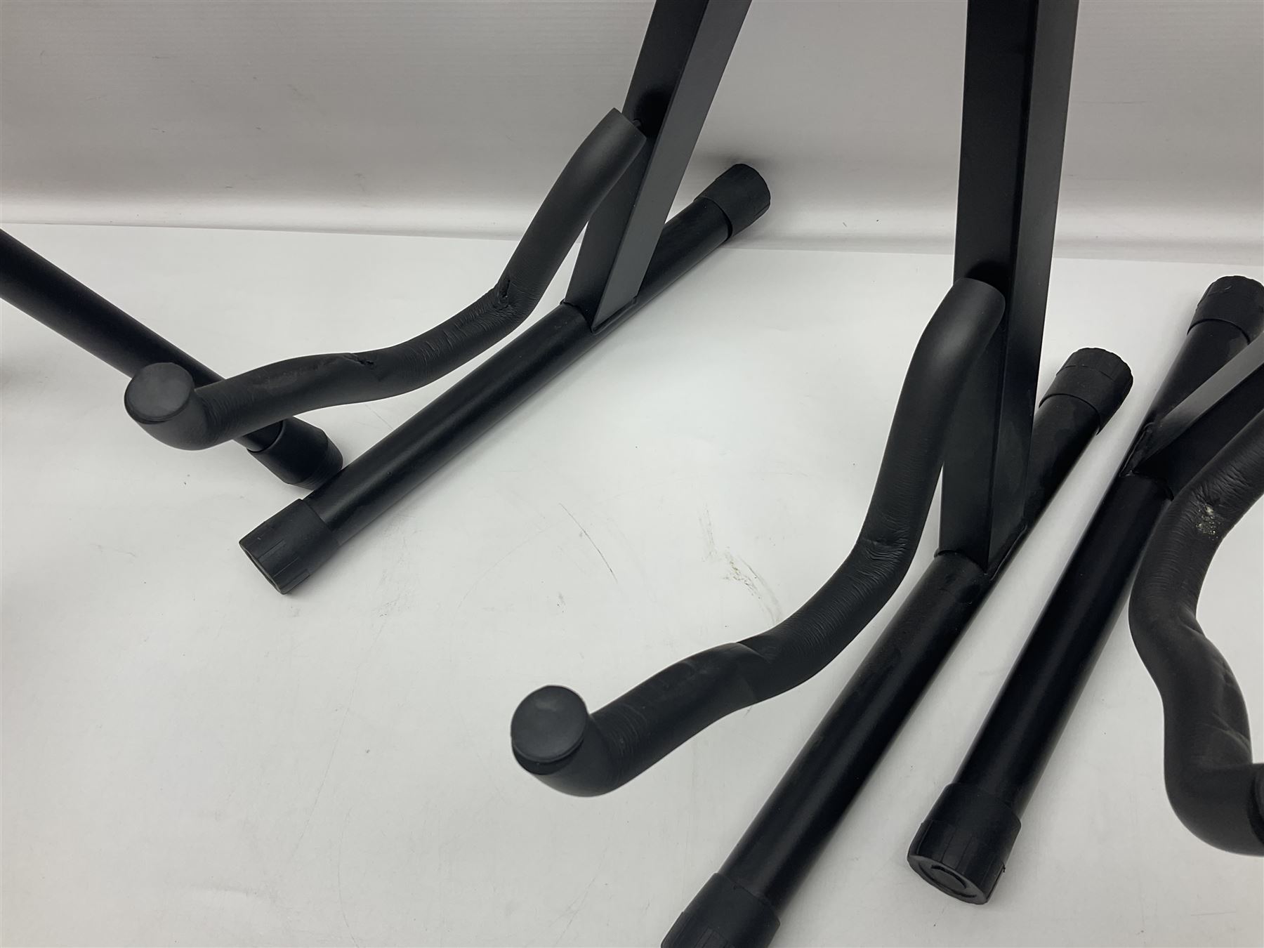 Four folding tubular guitar stands, two by RockJam; and folding tubular saxophone stand (5)