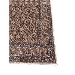 Persian Kirman carpet, the ivory ground field and border decorated with repeating Boteh motifs, interspaced with all-over floral design, blue ground border guards, the top border with signature panel