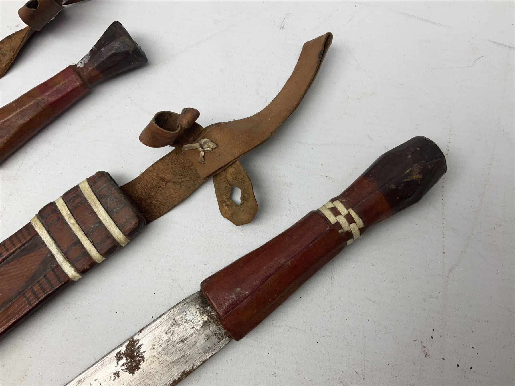 Indian kukri with 29cm curving steel blade and nickel mounted horn grip; in leather covered scabbard with one skinning knife L42cm overall; Hitler Youth knife with scabbard in relic condition; and three African graduated knives each with crudely carved wooden grips and painted leather covered scabbards (5)
