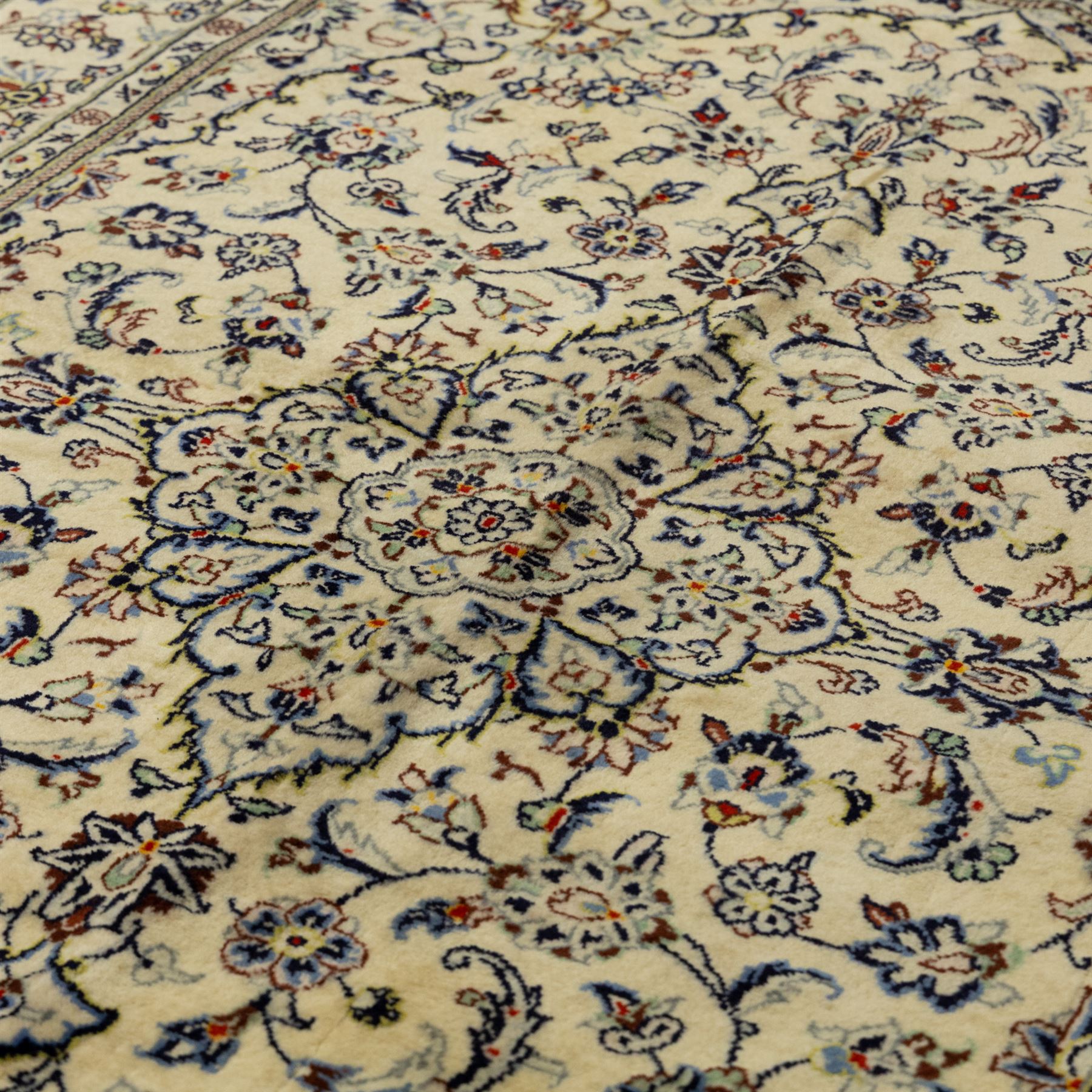 Central Persian Kashan hand-knotted rug, ivory ground, with a small central floral medallion and pendants, the field finely decorated with blue, cream and soft red scrolling vines, flowerheads and palmettes, within an ivory floral border and narrow guard stripes, with cotton fringes