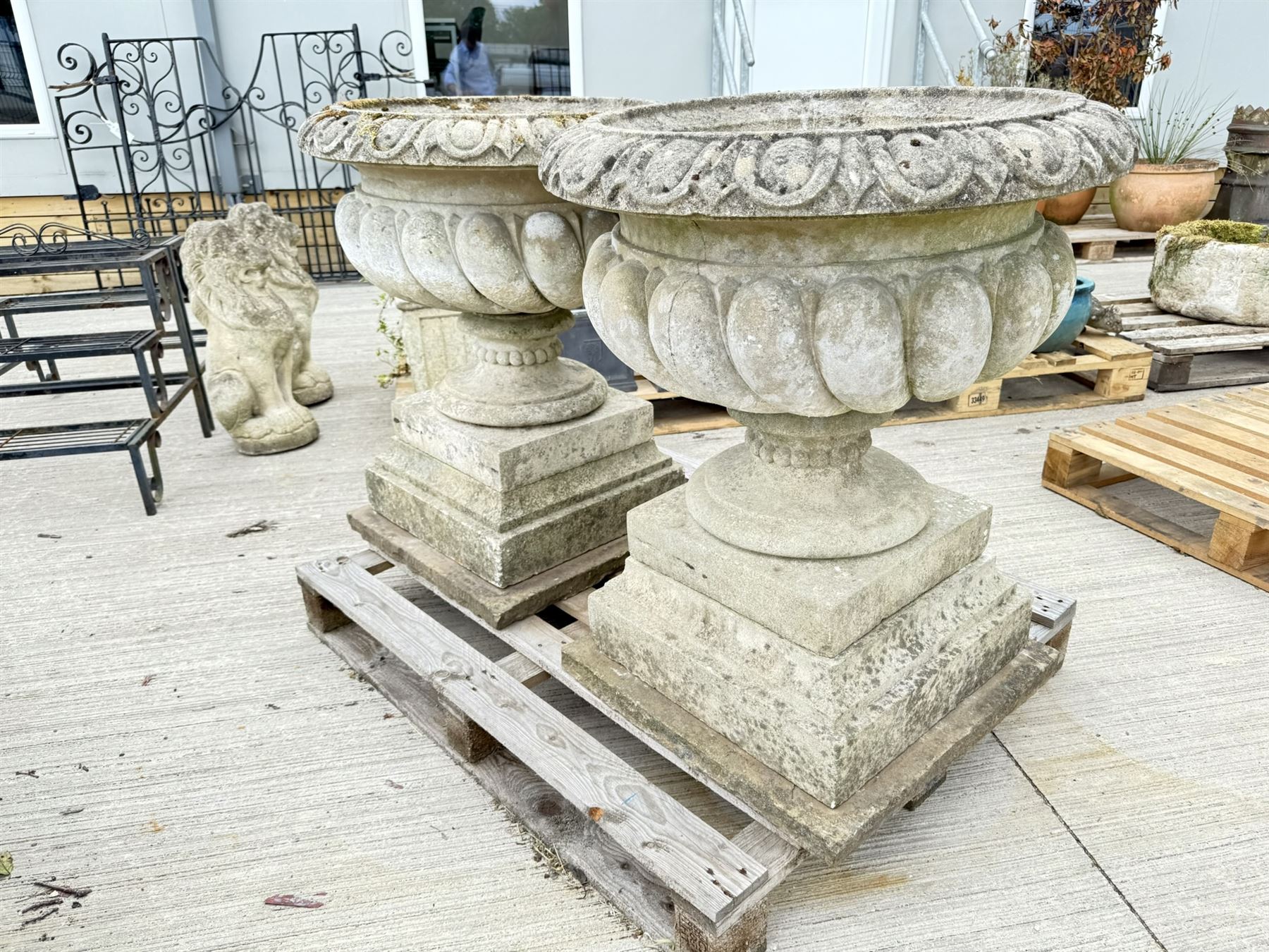 Pair of large weathered Country House Haddonstone garden urns, acanthus carved rim above gadrooned bowl, beaded detailing to the neck, raised on stepped double plinth base
