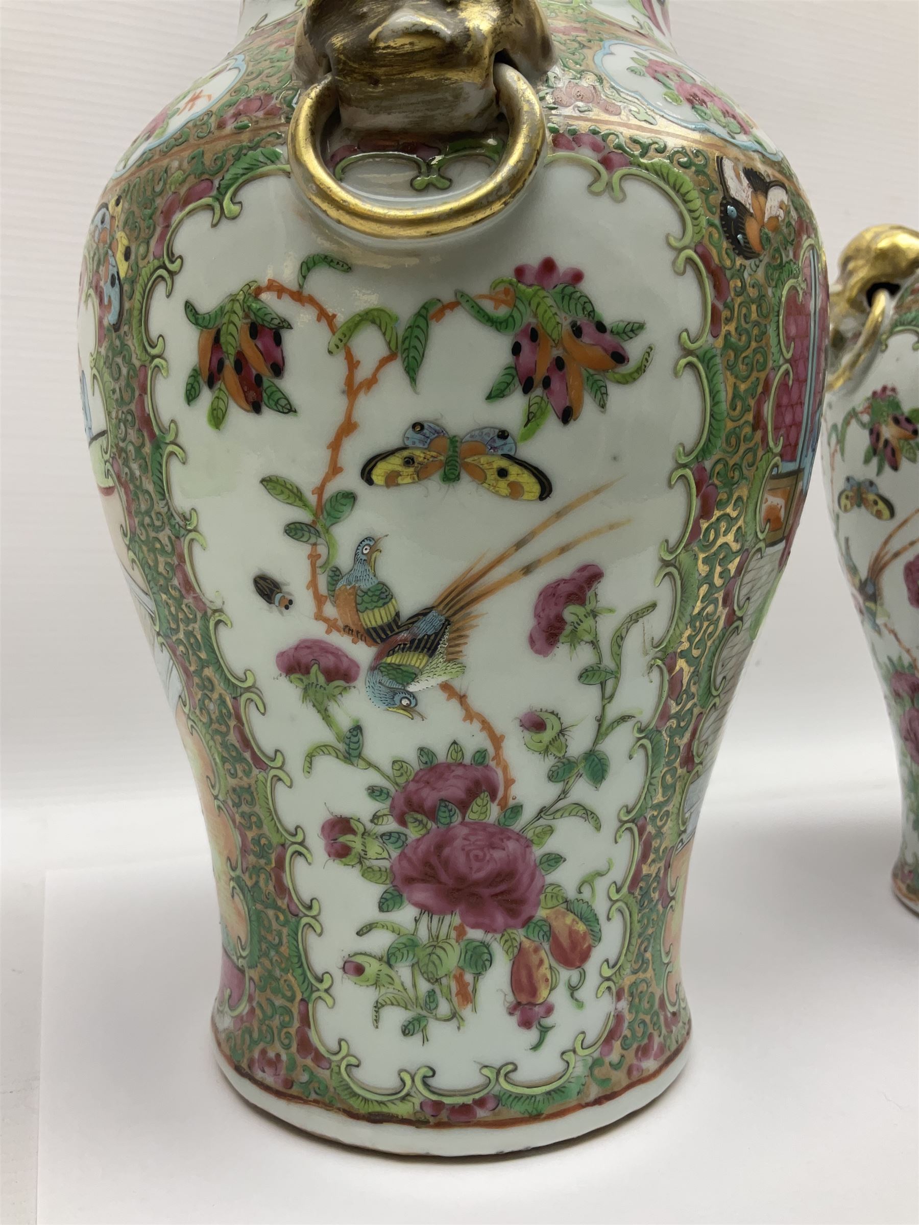 Pair of 19th century Chinese Famille Rose vases and covers, each of baluster form with twin gilt lion mask ring handles to shoulders, the flattened domed covers with gilt temple lion finials, each decorated with alternating reserves of bijin and attendants, and birds and butterflies amongst blossoming peonies, against a gilt ground profusely decorated with stylised scrolls, H32.5cm