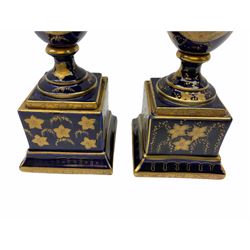 Pair of Vienna style urns, of ovoid form with twin gilt handles, upon a spreading circular foot and plinth base, the bodies decoration with oval panels of dancing classical figures, the whole heightened in gilt, with spurious mark beneath, H21cm