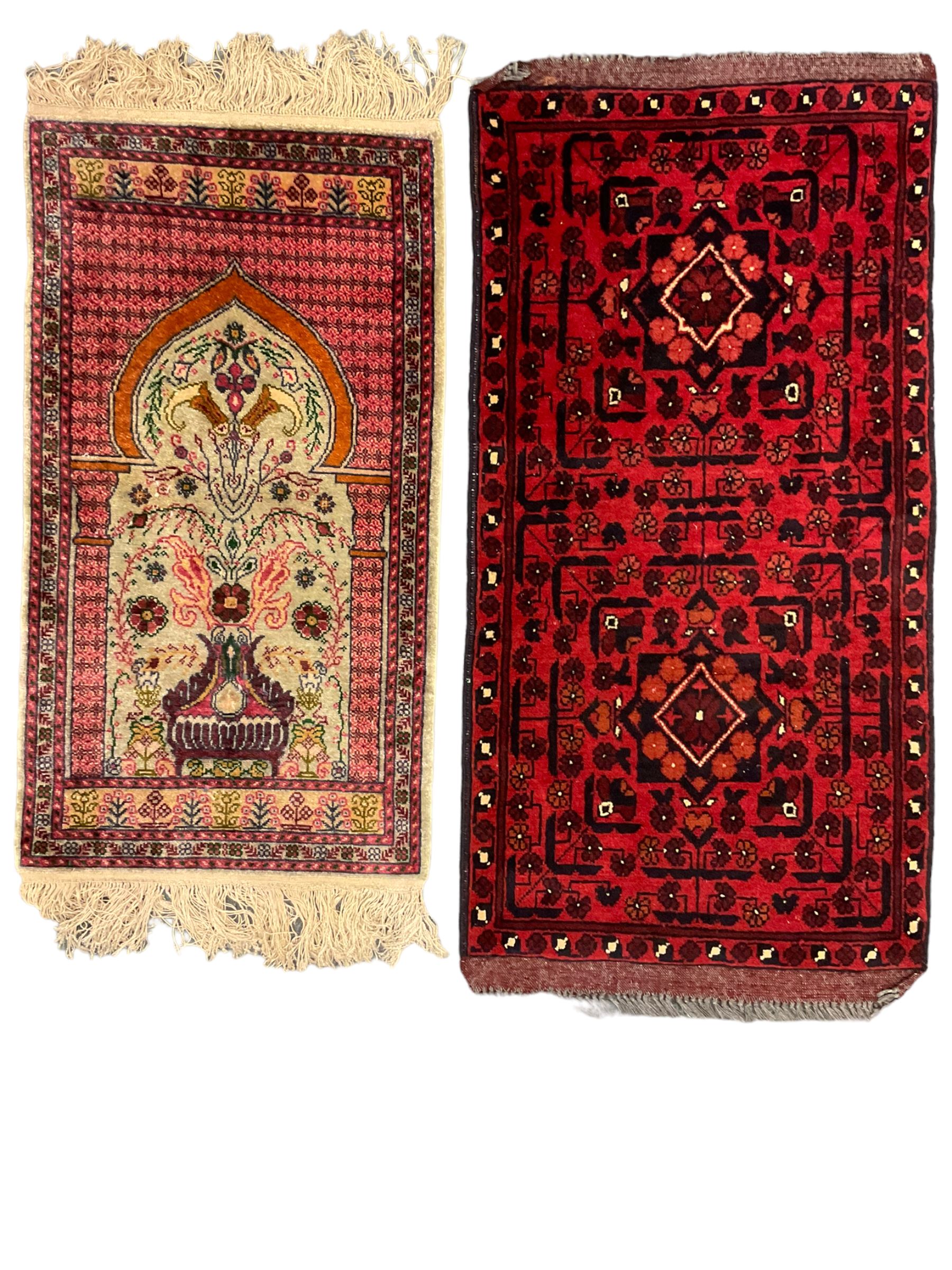 Small Persian magenta ground rug, central Mirab with flanking columns enclosing stylised urn motif with trailing foliage, the triple band border with plant motifs (86cm x 46cm); Persian red ground rug, two central floral medallions with extending flower heads, floral decorated border (106cm x 53cm) (2)