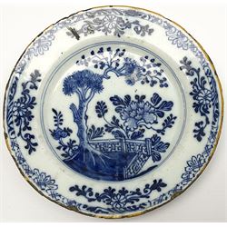 Three English Delftware plates, each decorated with a Chinese inspired scene with peonies, fir trees, and fence, smallest example with ochre rim line indistinctly signed beneath, largest D22.5cm, smallest D19.5cm