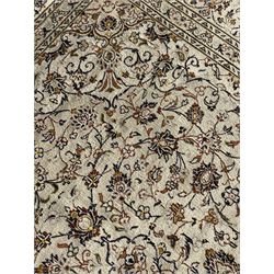 Persian Kashan ivory ground carpet, central medallion decorated with sixteen arranged palmette motifs, within a field decorated with swirling leafy branches and stylised plant motifs, the main border decorated with matching swirling pattern, within floral pattern guard stripes 