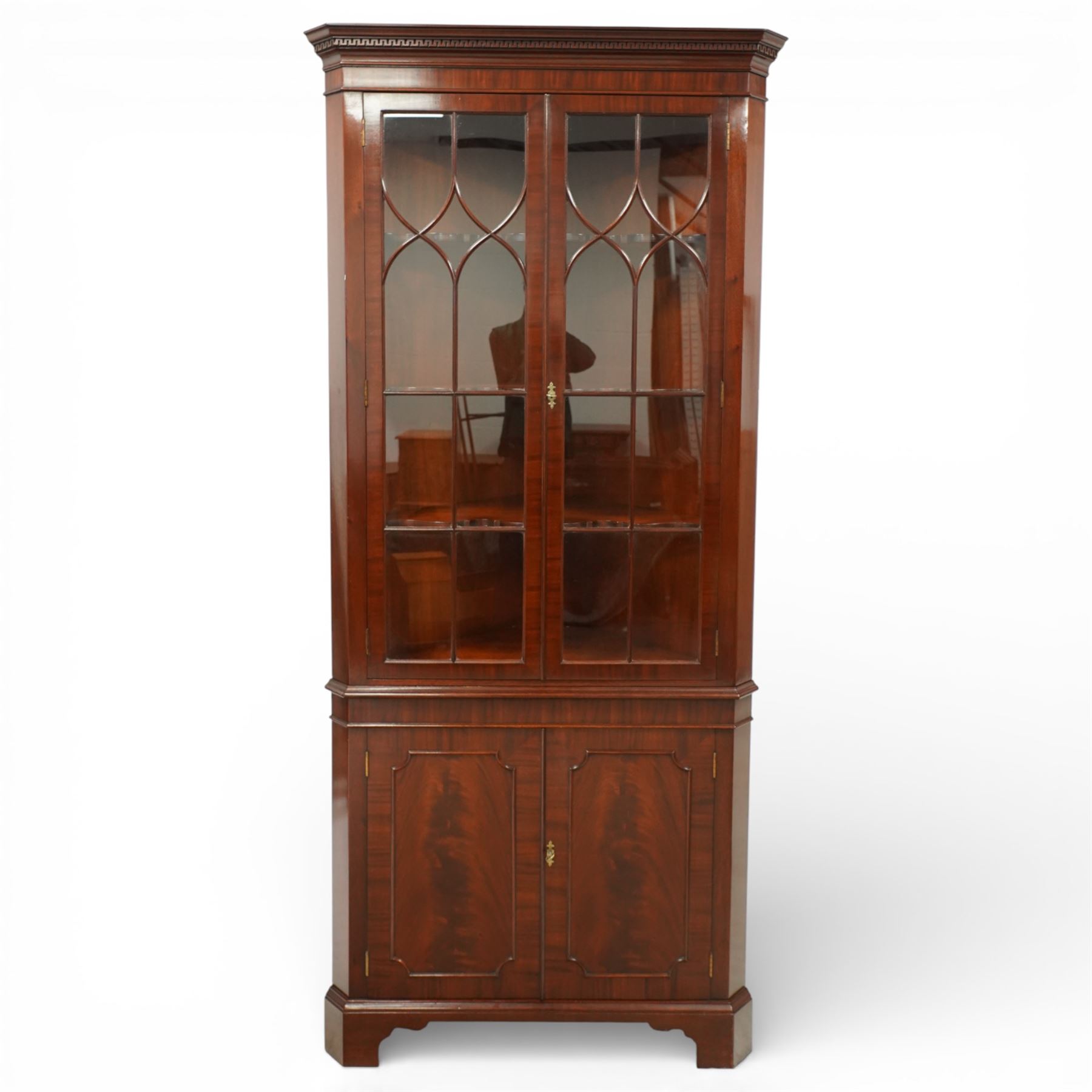 William Tillman - Early 20th century mahogany corner cabinet, the projecting moulded cornice with dentil detail over a glazed upper section enclosed by a pair of astragal glazed doors with Gothic arched tracery, the interior fitted with shaped shelves, above a moulded waist and a lower cupboard enclosed by two panelled doors with shaped fielded panels, raised on bracket feet