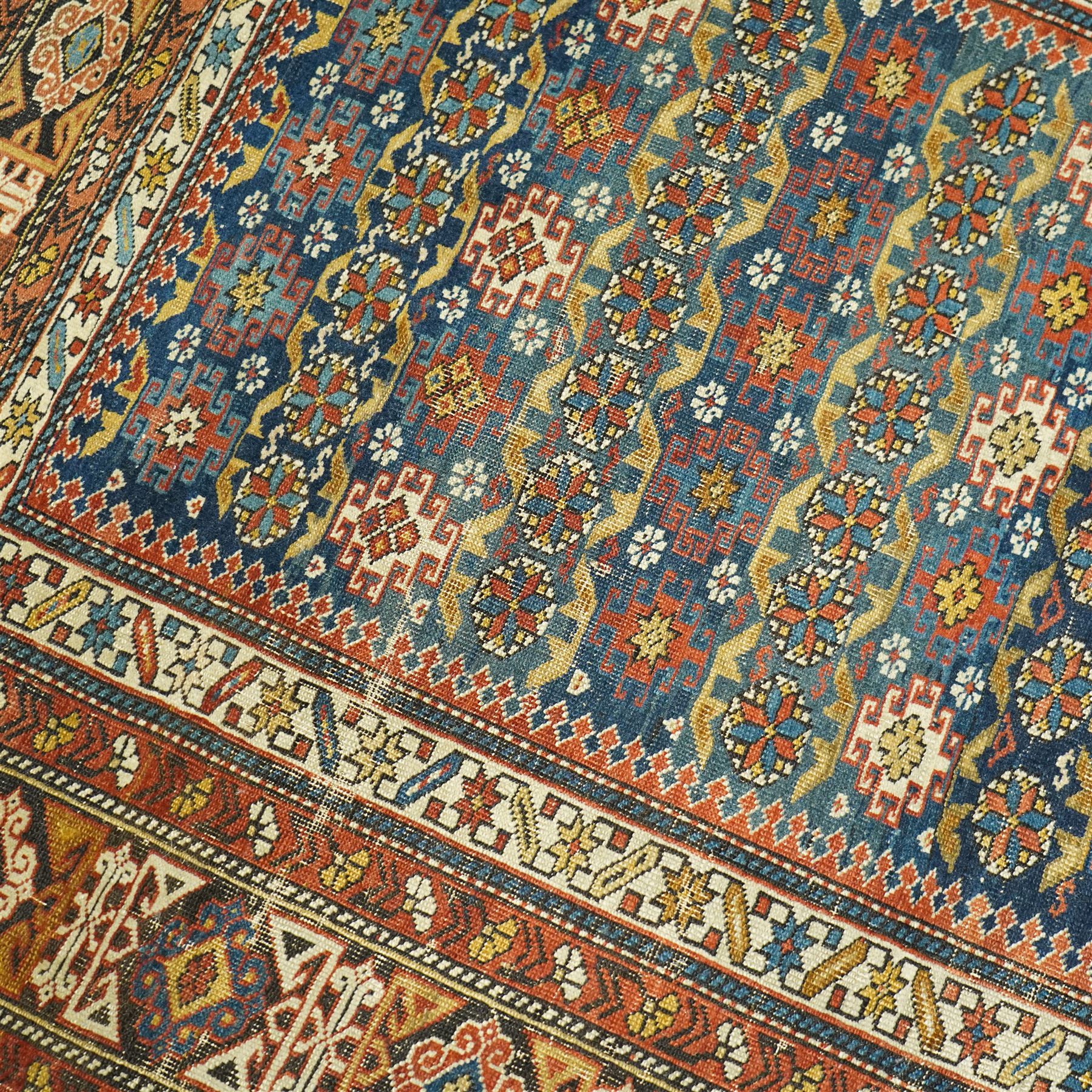 Two antique Caucasian Shirvan rugs, indigo field decorated with horizontal bands of small geometric floral and star motifs within multiple finely drawn borders featuring diamonds, rosettes, and stylized leaves in a palette of madder red, ivory, ochre, and pale blue, with fringe ends, 195x137cm, together with a similar smaller rug, 143x96cm