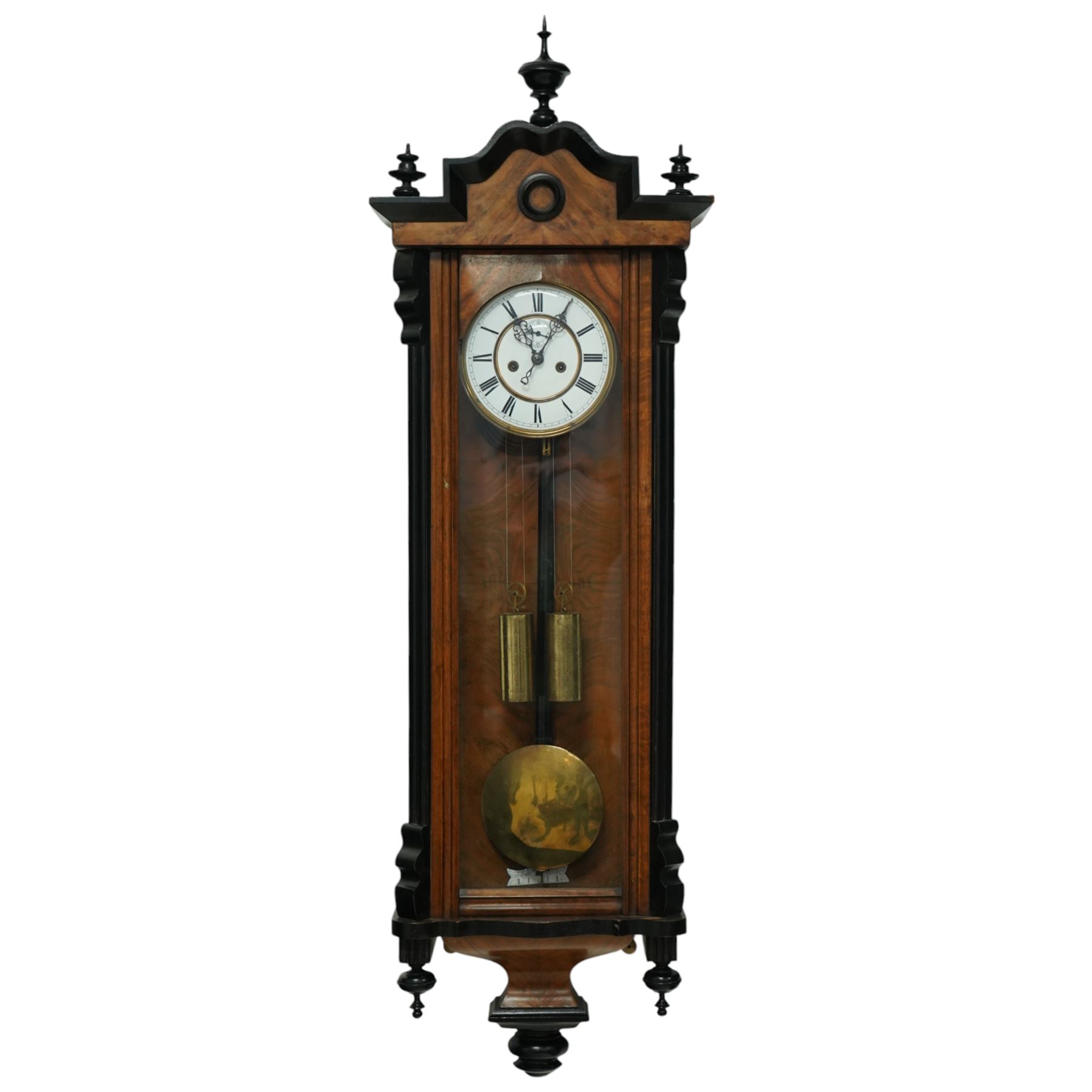German- Late 19th century twin weight 8-day Vienna wall clock, in a walnut and ebonised case with turned finials and pendants, fully glazed door displaying the the brass cased weights and pendulum, enamel two-part dial with Roman numerals, minute rack, seconds hand and gothic steel hands, rack striking movement with a deadbeat escapement, striking the hours and half-hours on a coiled gong. With key.