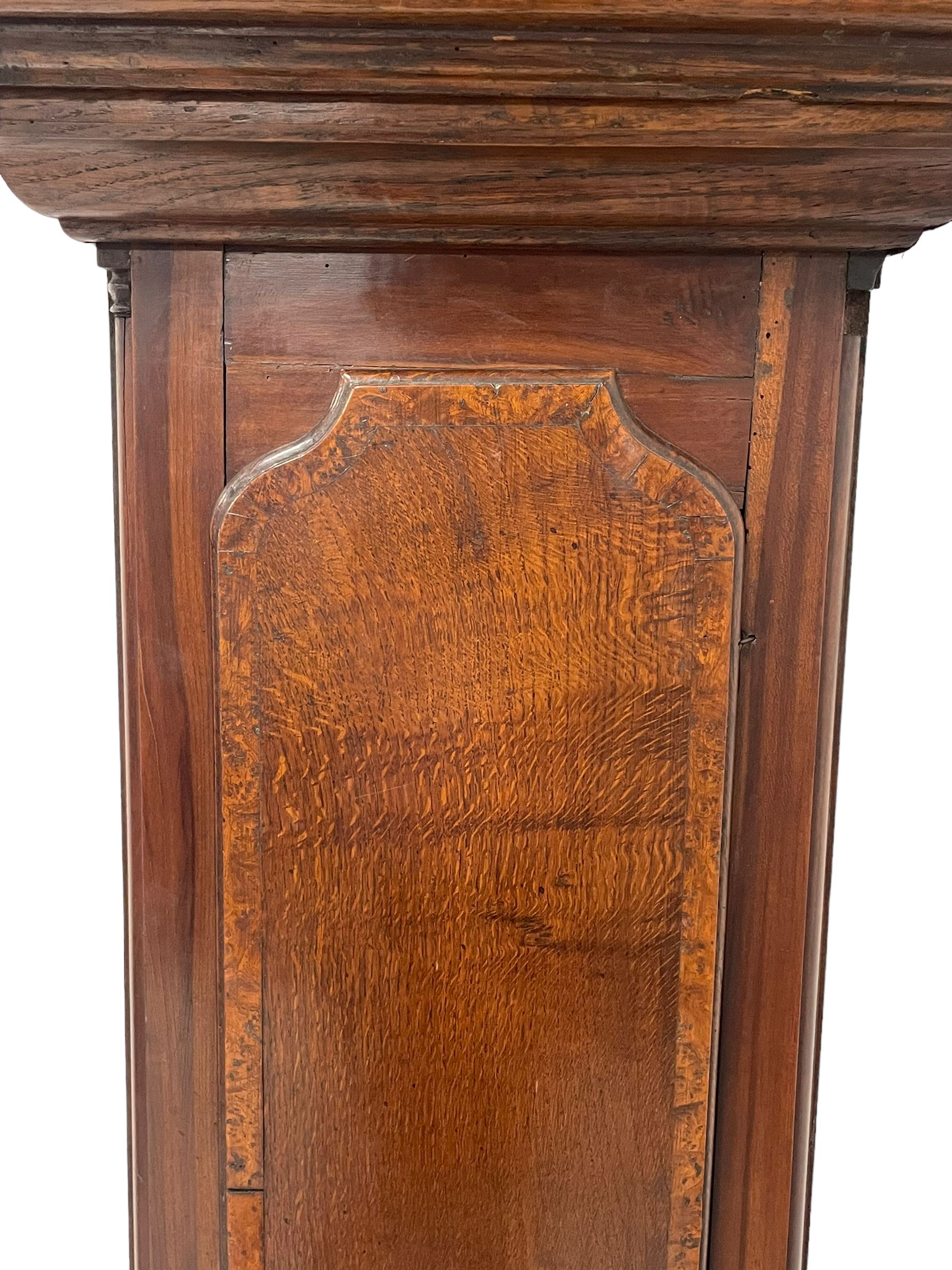 John Watts of Canterbury - early 18th century 8-day oak longcase clock, with a flat topped hood, broad cornice, dentil moulding and blind fret beneath, baluster turned pilasters with wooden capitals flanking the square hood door, trunk with recessed beaded edge and a long ogee topped door with crossbanding, plinth with applied skirting, square brass dial with matching steel hands, cast spandrels and a matted and engraved centre, date aperture, seconds ring and ring turned winding apertures, silvered chapter ring with Roman numerals, five minute Arabics, minute and quarter hour tracks, five pillar movement with a recoil anchor escapement and inside countwheel strike, sounding the hours on a bell. With weights and pendulum.