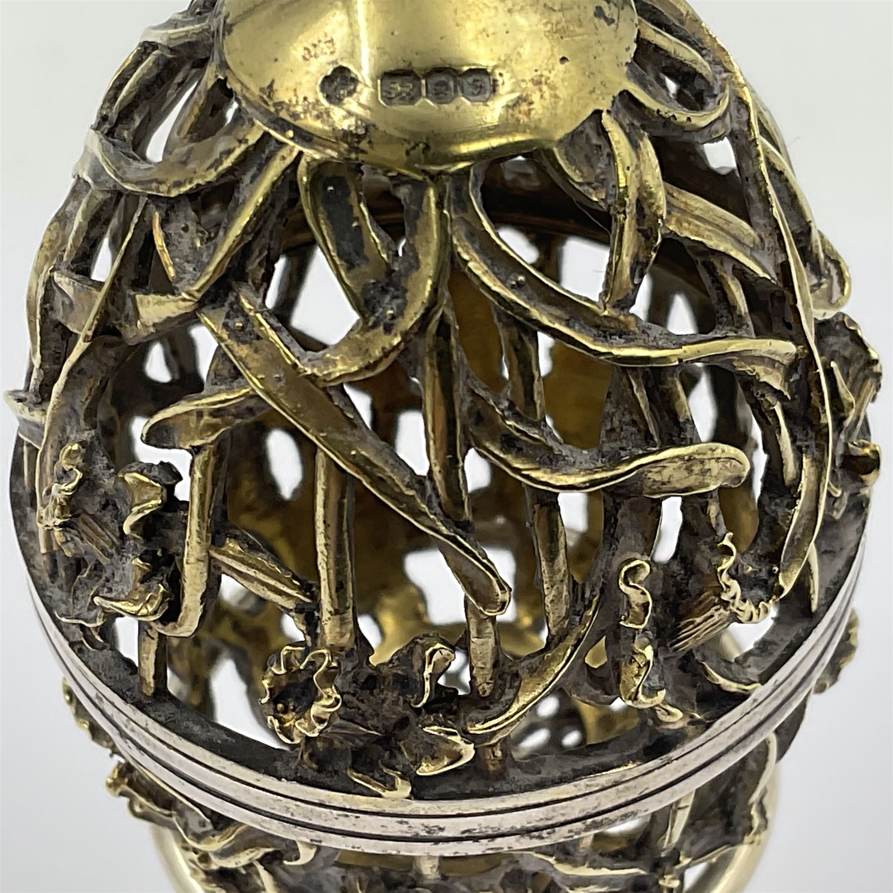 Modern silver limited edition Easter egg, no. 70/500, the gilt openwork body decorated with daffodils and detachable cover with pierced circular panel set with a single faceted blue stone, opening to reveal a gilt interior, upon silver stand with three scrolling pad feet, each hallmarked St James House Company, London 1980, height including stand 8cm