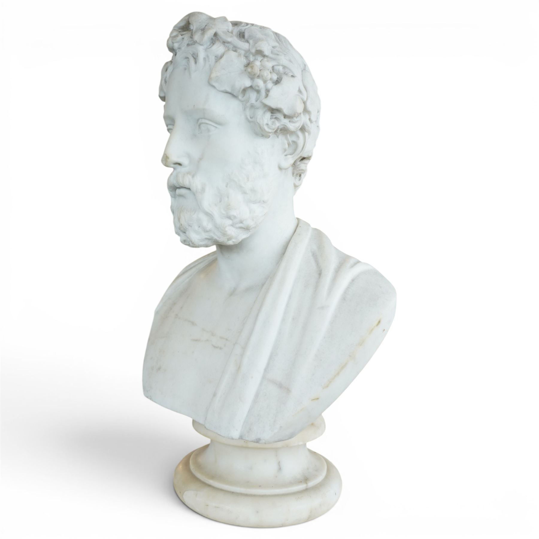 Aristide Louis Fontana (Italian 1834-1907): Grand Tour marble bust of a Roman emperor, probably inspired by portraits of Marcus Aurelius, portrayed with finely carved curled hair and beard beneath a grapevine wreath with trailing vine leaves and clusters of fruit, the draped shoulders and truncated chest raised upon a turned circular socle, signed to the reverse, H61cm; together with the associated faux marble pedestal of rectangular form, H94cm
Provenance: Kirkham Hall