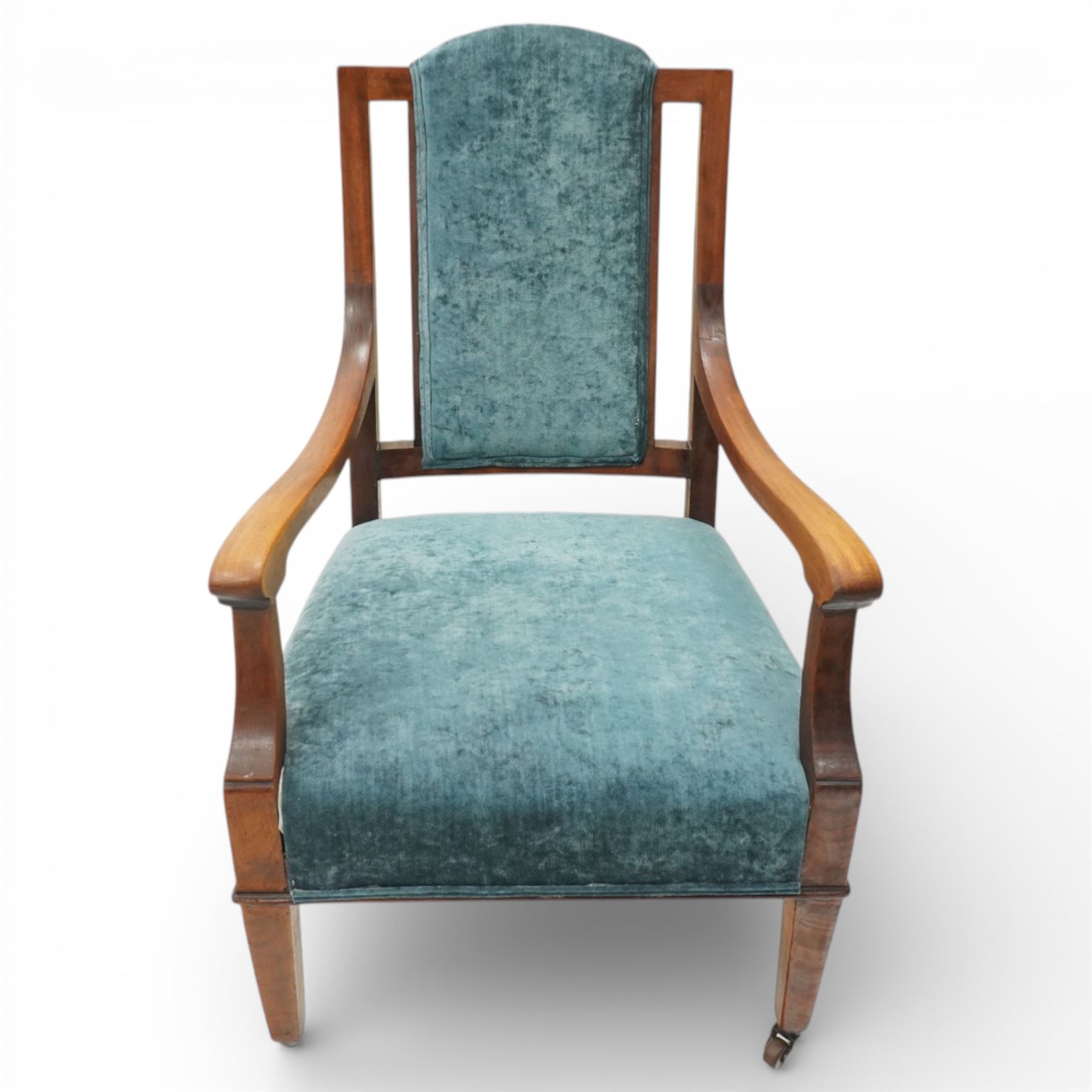 Arts & Crafts mahogany framed armchair, shaped rectangular back with open uprights, padded back, seat and arm supports upholstered in blue velvet, downswept arms on square tapering front supports with brass caps and castors, the rear supports slightly splayed