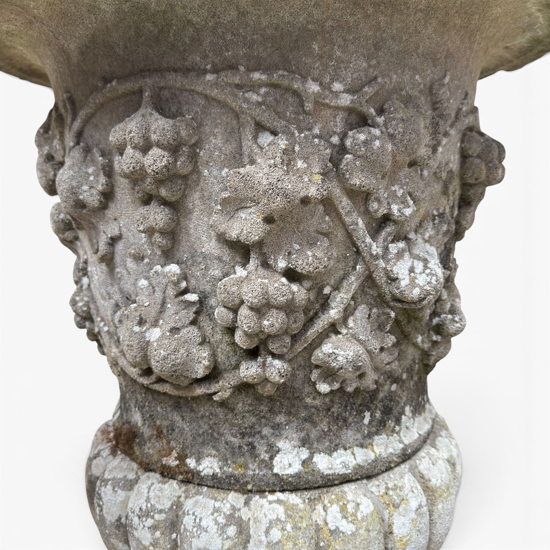 Pair of quality antique weathered three-piece composite stone garden urns, the flared rim moulded with repeating acanthus leaves, over a deep-relief campana body decorated with fruiting grapevines and ivy leaves, the gadrooned underbelly over a turned socle and square base