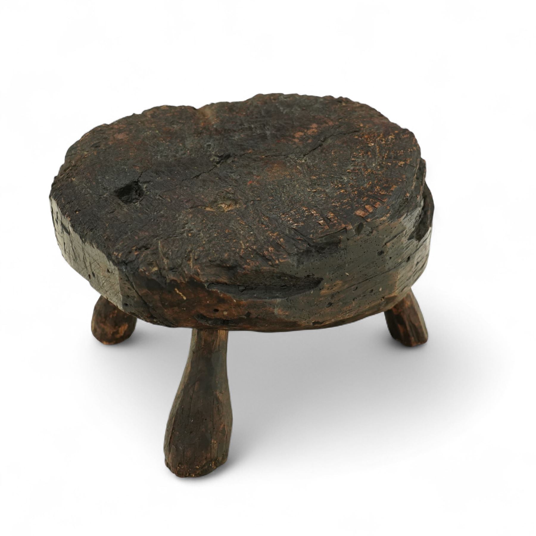Rustic bog oak stool of oval form with a single solid section with a deeply patinated and textured surface, raised on three tapered stick legs, possibly Irish 