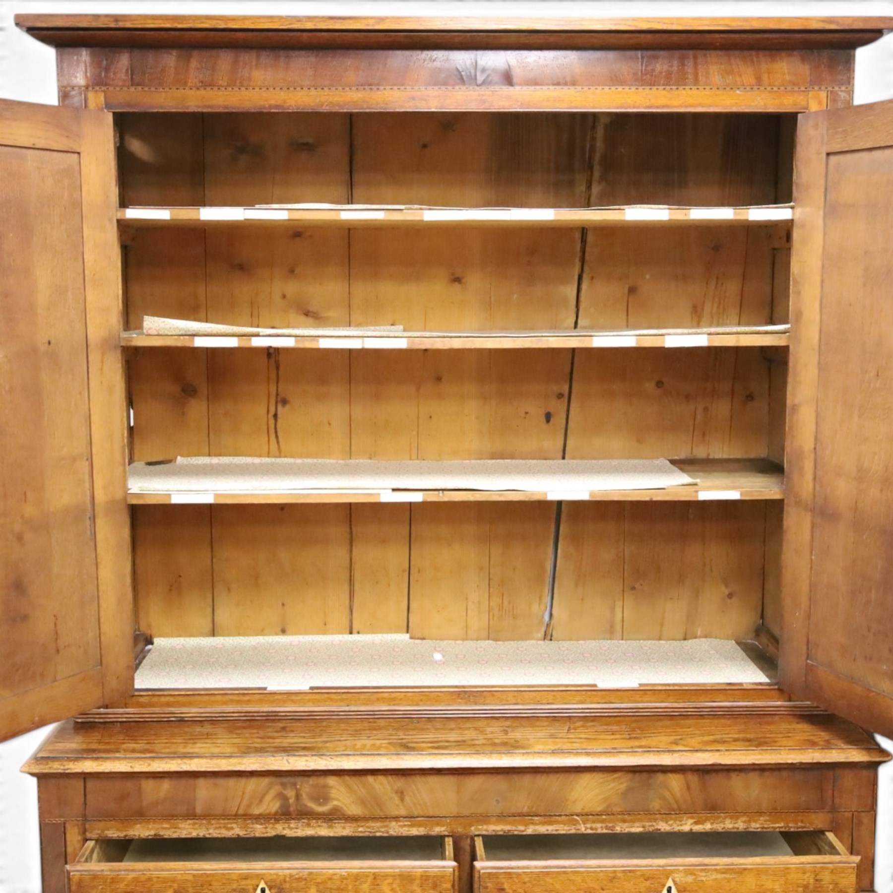 Georgian oak and mahogany housekeepers cupboard, the upper section with projecting cornice, crossbanded and inlaid frieze, above panelled doors with bone escutcheons, enclosing three fixed shelves, flanked by barley twist quarter pilasters, the lower section with further crossbanded and inlaid frieze, two short over two long graduating drawers with ebonised handles, raised on turned supports 