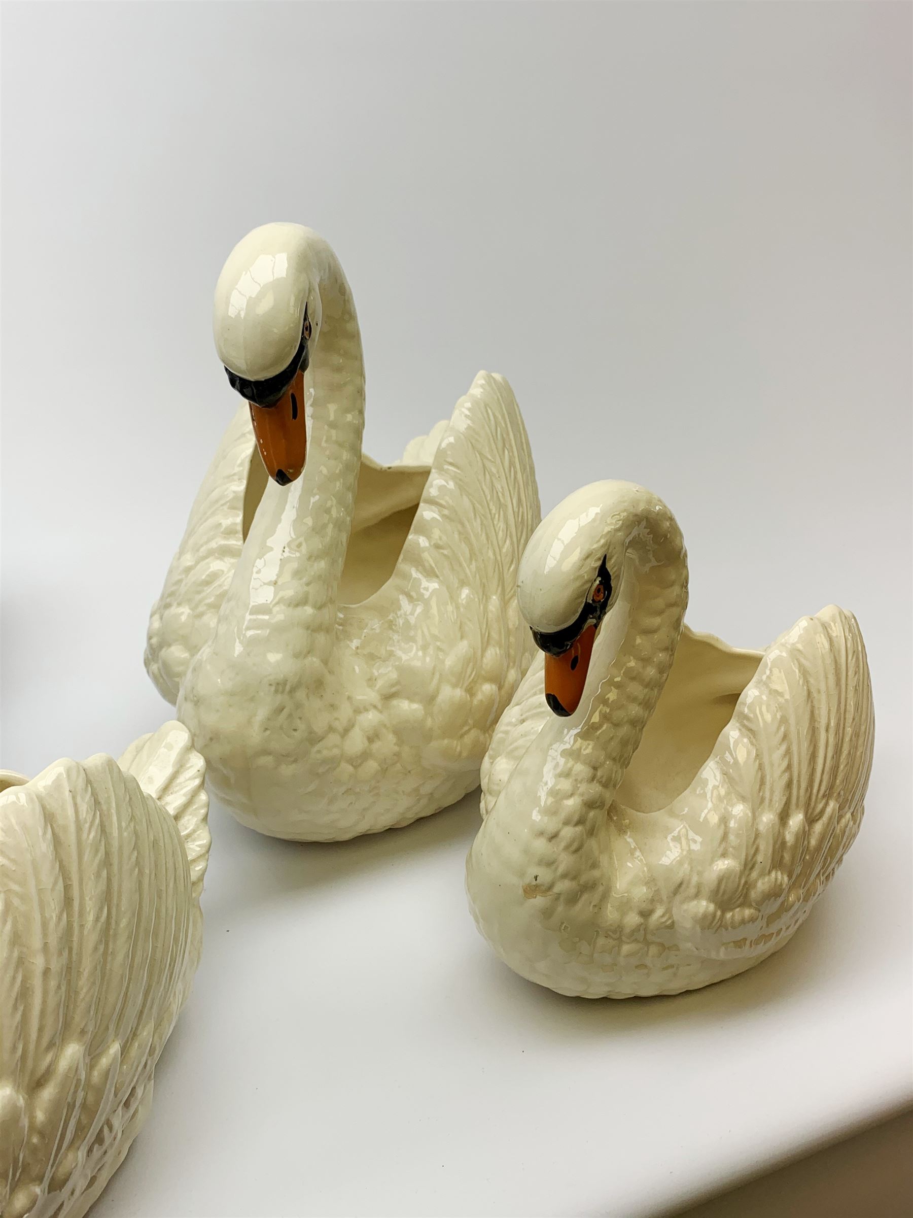 Four Dartmouth pottery jardinières or planters, modelled in the form of swans, comprising three white examples, and one black, marked beneath Dartmouth Devon England, larger examples H29cm, smaller examples H21.5cm. 