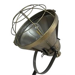 Industrial tripod spotlight, with a metal shade and wire guard, supported by a height-adjustable tripod base, the head equipped with an adjustable tilt mechanism