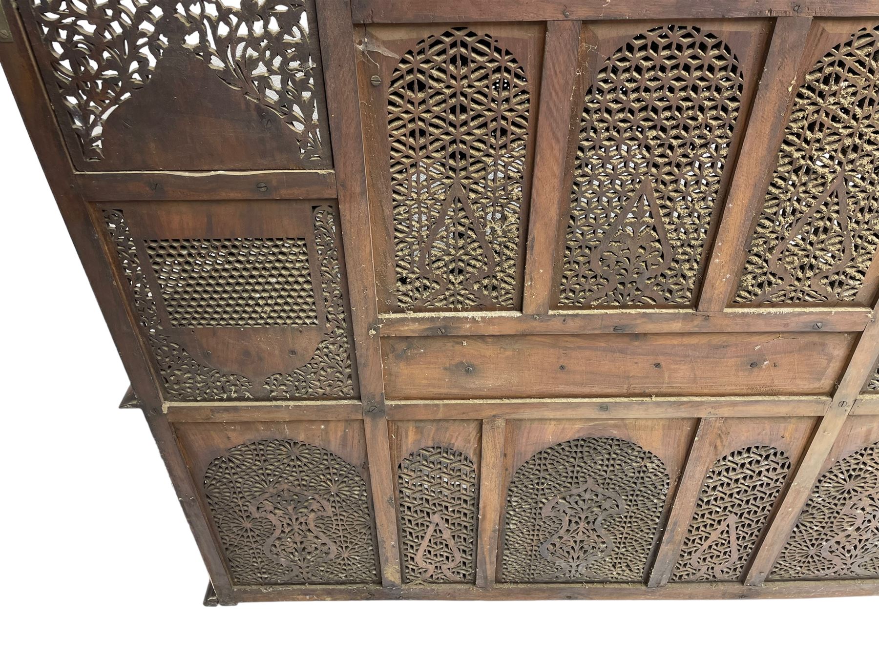 Late 19th century Indian Burmese carved and pierced hardwood and brass inlaid wall shelf, the shaped back profusely decorated with trailing and interlaced foliage, with projecting architectural structures, the central balcony with canopy top and five open windows with arched apertures on columns, two flanking five-sided balconies, the shelf supported by six foliate carved columns with pierced cusped pointed arches 