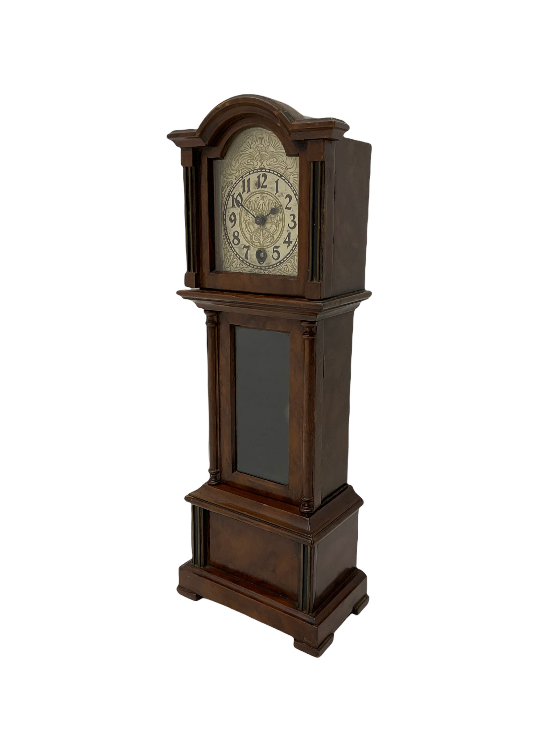A miniature spring driven longcase clock made in Germany by the Hamburg American Clock Company c 1890, with a mahogany finished case, break arch pediment and opening hood door, case with a fully glazed opening trunk door on a short plinth with raised feet, with an etched silver effect dial, Arabic numerals, minute track and spade hands, 8-day key wound movement with a silk suspension and visible pendulum.





