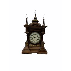 A late 19th century German Black Forrest mantle clock striking the hours and half hours on a coiled gong, two-piece white enamel dial inscribed with the six pointed Junghans logo, roman numerals and minute track, steel spade hands, spun brass bezel and glass, spring driven eight day movement with a recoil anchor escapement, carved oak case in fantasy form, multi-stepped plinth with incised brickwork effect to the sides and front of the case, with applied brass ornamentation, projecting turrets and gun ports, case surmounted with a pediment consisting of three distinctively carved oriental domes with roof tiles and guidon banner flags.
With pendulum.
