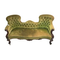 Victorian rosewood framed serpentine settee, upholstered in buttoned laurel green fabric with sprung seat, scrolled arms with carved foliate decoration, apron carved with central cartouche, raised on cabriole supports with brass castors