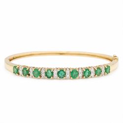 14ct gold emerald and diamond hinged bangle, nine oval cut emeralds, each spaced by two ro...