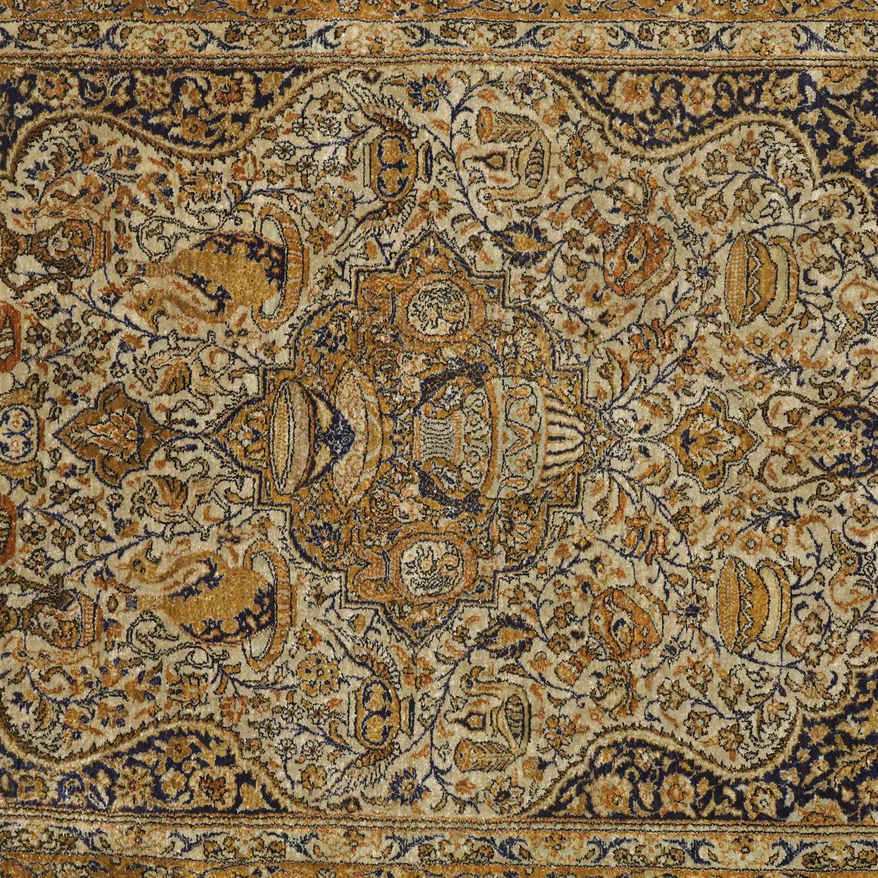 Persian Kashan design silk and wool blended rug, with a central medallion incorporating vases and scrolling floral motifs, set against a dark blue and ivory ground within a patterned border, some fraying to end fringes