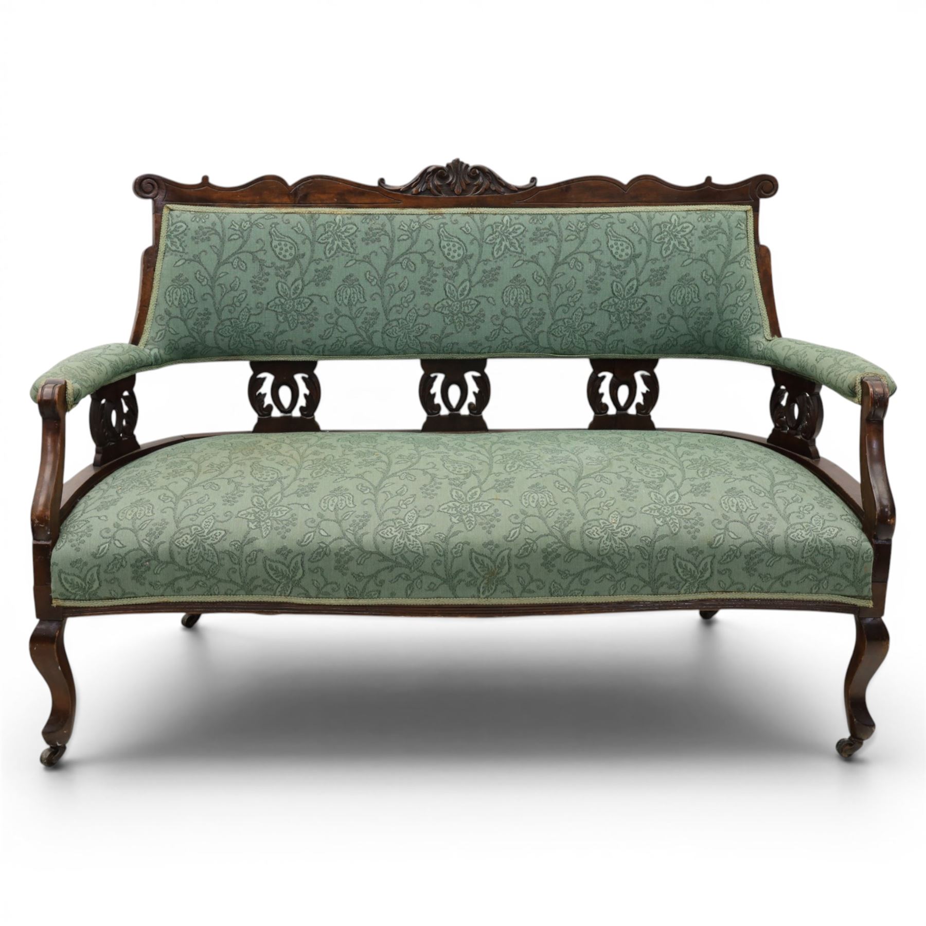 Edwardian mahogany framed sofa, shaped cresting rail with scroll terminals and carved foliate pediment, upholstered back and swept arms in green foliate fabric, pierced splat supports, serpentine front seat rail, on cabriole supports terminating in castors