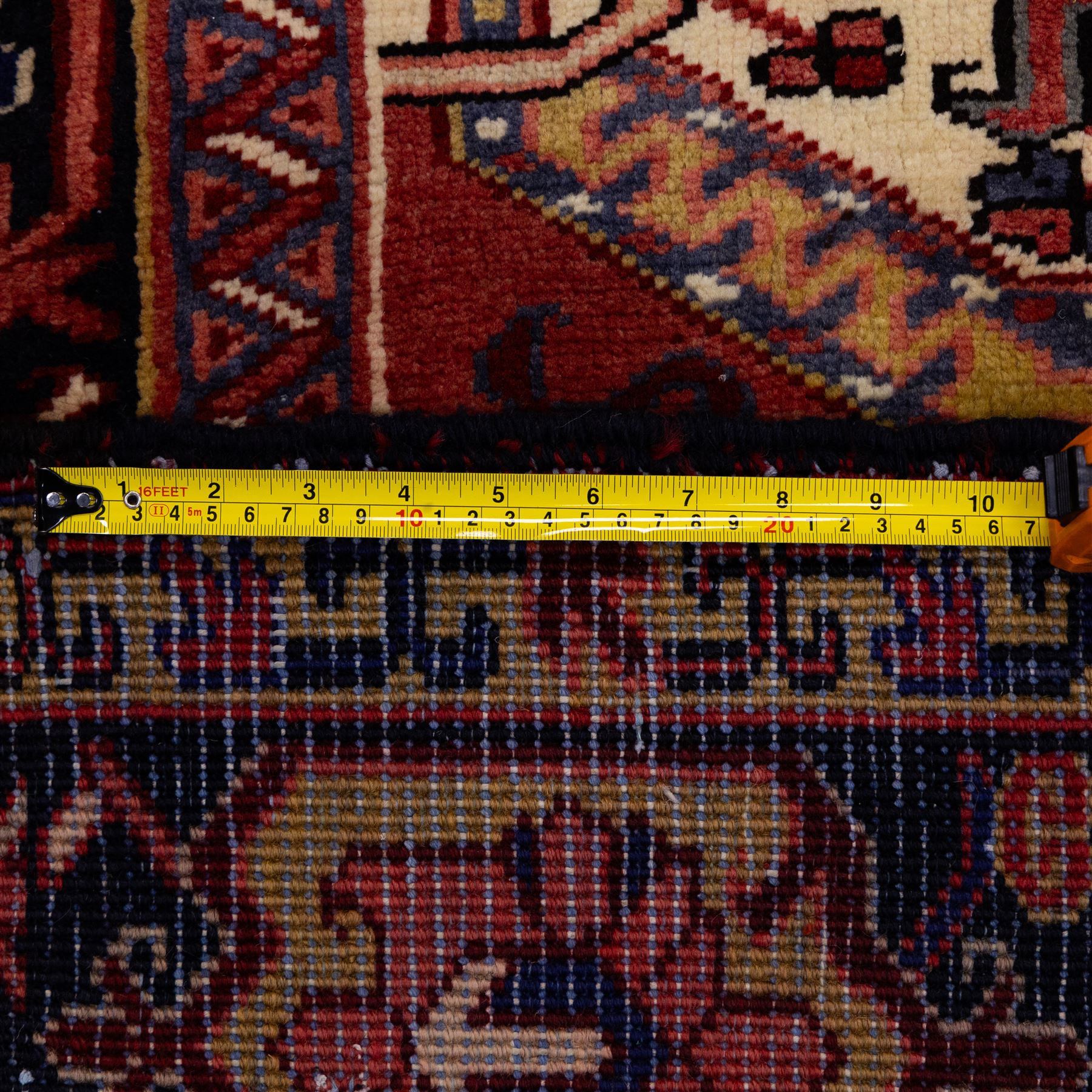 North West Persian Heriz hand-knotted carpet, madder red field with large central stepped medallion with angular floral and geometric designs, surrounded by stylized palmettes, leaves and tribal motifs with indigo corner spandrels, enclosed by a broad navy border of geometric floral devices between multiple guard stripes, with cotton fringe ends 