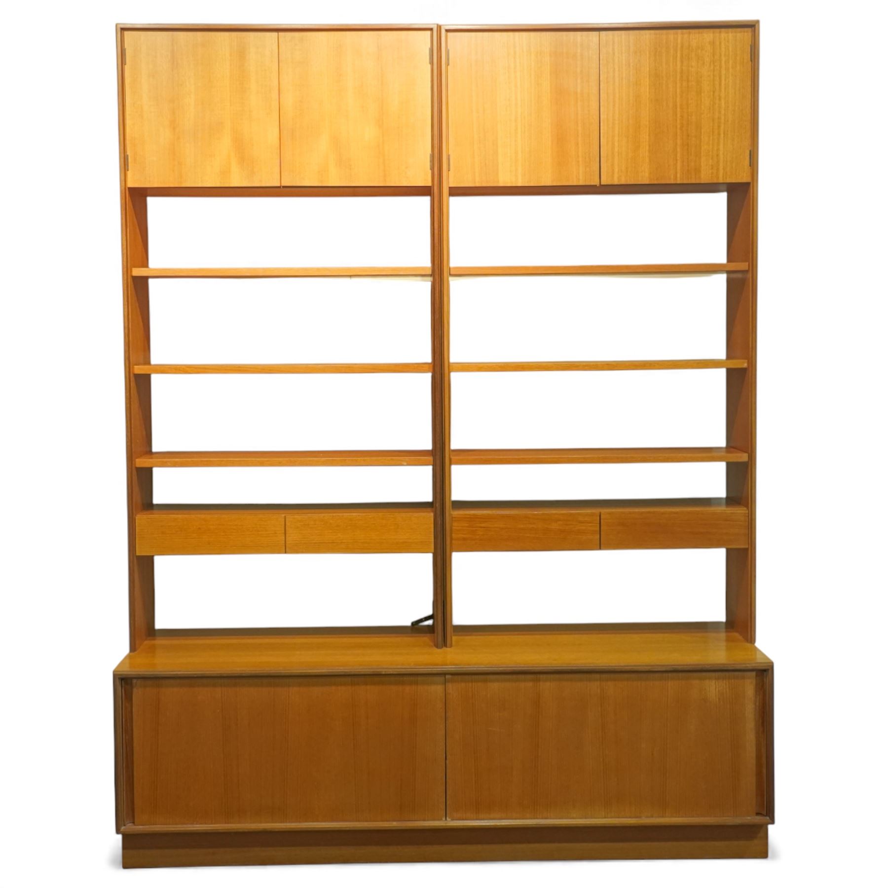 G Plan - 'Form 5' teak modular bookcase unit, comprising two upright sections with upper cupboard compartments enclosed by hinged doors, open adjustable shelving below, fitted with a pair of central drawers to each section, raised over a long base cabinet with sliding cupboard doors