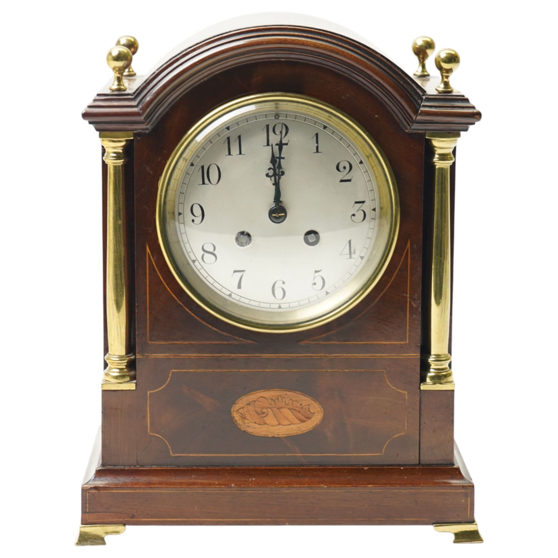 Edwardian-French mahogany cased mantle clock c1910 in a break-arch case with brass finials and recessed brass columns, with inlaid satinwood stringing and conche inlay to the front, raised on a short plinth with bracket feet, twin train movement with rack striking, sounding the hours and half-hours on a coiled gong.
With pendulum and key.