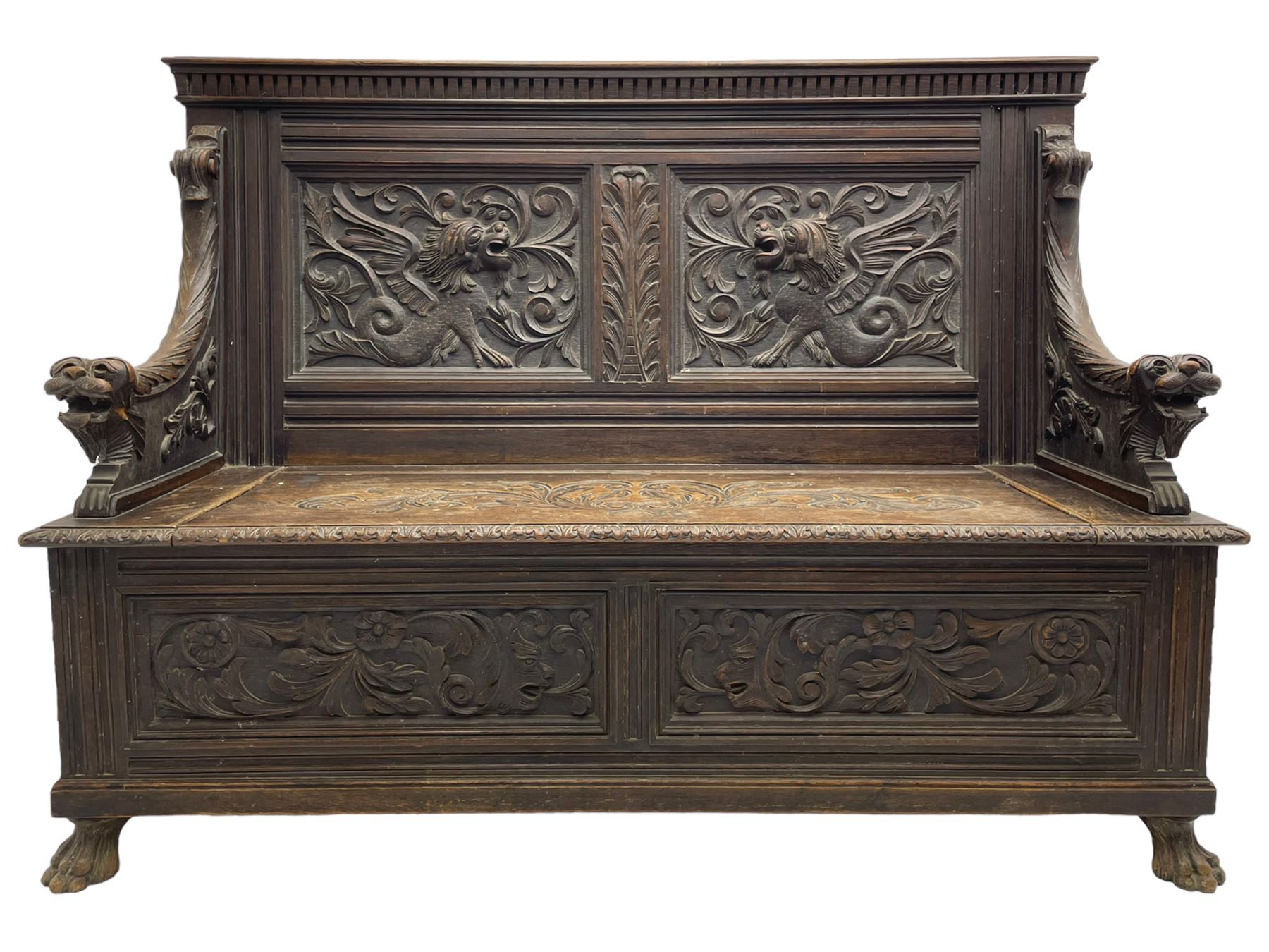 19th century oak hall bench, dentil cresting rail over moulded frame with panelled back carved with fire-breathing mythical beasts and central acanthus leaf motif, scroll carved down-sweeping arms carved with grotesque masks with scrolled foliage and shells, hinged box seat carved with scrolling foliage over panelled front with further carved foliage decoration, on paw carved front feet 