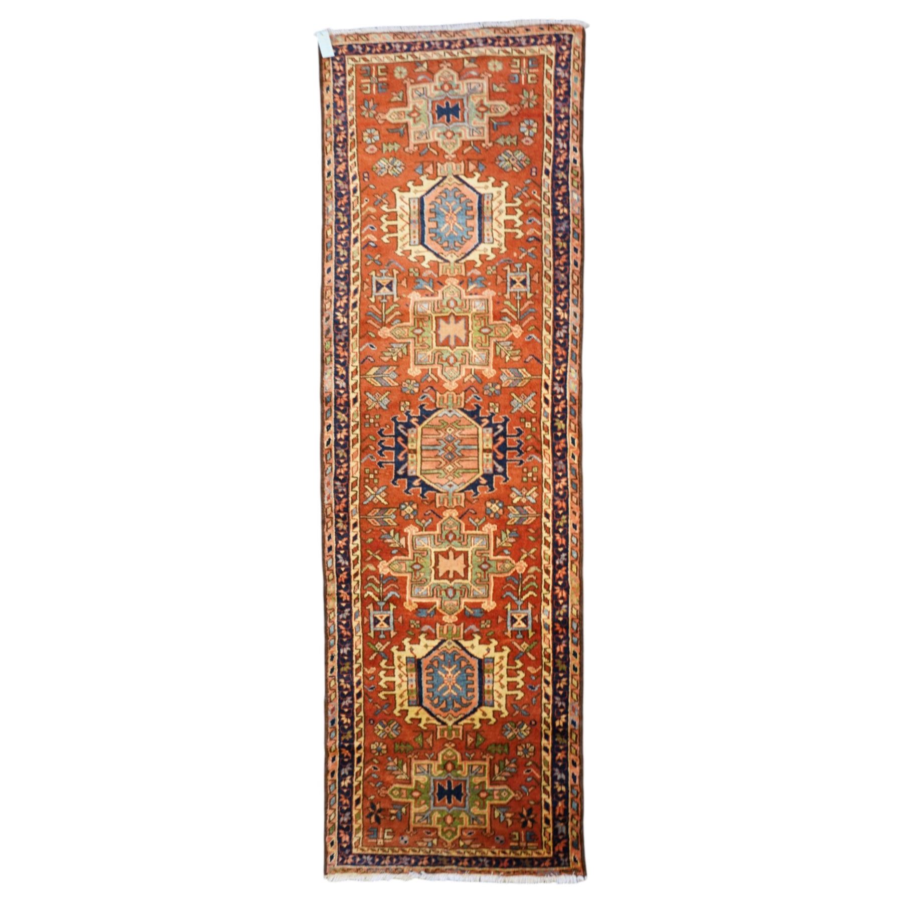 North West Persian Karajeh hand-knotted runner, field decorted with a series of linked stepped hexagonal medallions encloing stylized geometric motifs, surround by angular floral and tribal devices on a terracotta red ground enclosed a navy main border of repeating geometric and rosette motifs, between multiple guard stripes, with cotton fringe ends 