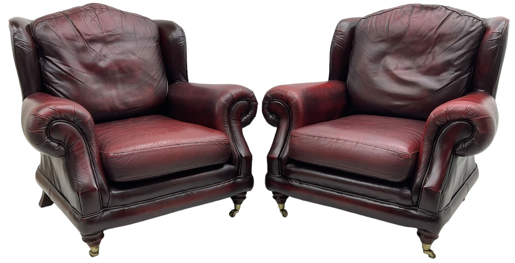 Thomas Lloyd - three-piece lounge suite, comprising of traditional shape two seat sofa (W190cm H80cm) and a pair of wingback armchairs (W100cm H91cm), each with rolled arms over turned supports with brass castors, upholstered in oxblood red leather
