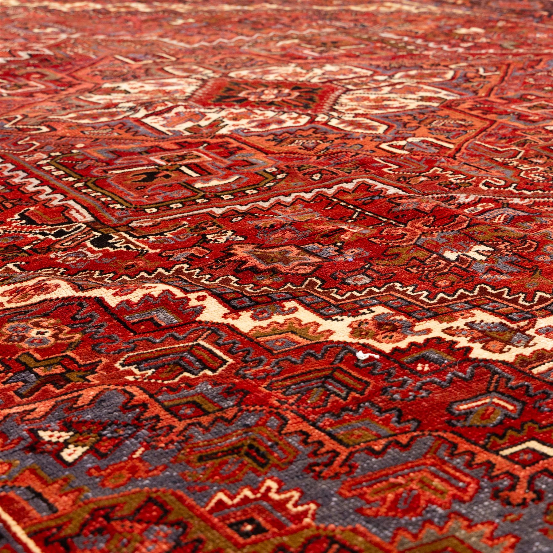 North West Persian Heriz hand-knotted carpet, madder red field, with a large central angular star medallion with stepped outlines on ivory ground, surrounded by geometric floral devices and stylized rosettes, with corresponding corner spandrels, enclosed by a bold geometric main border with multiple guard stripes, with cotton fringe ends 
