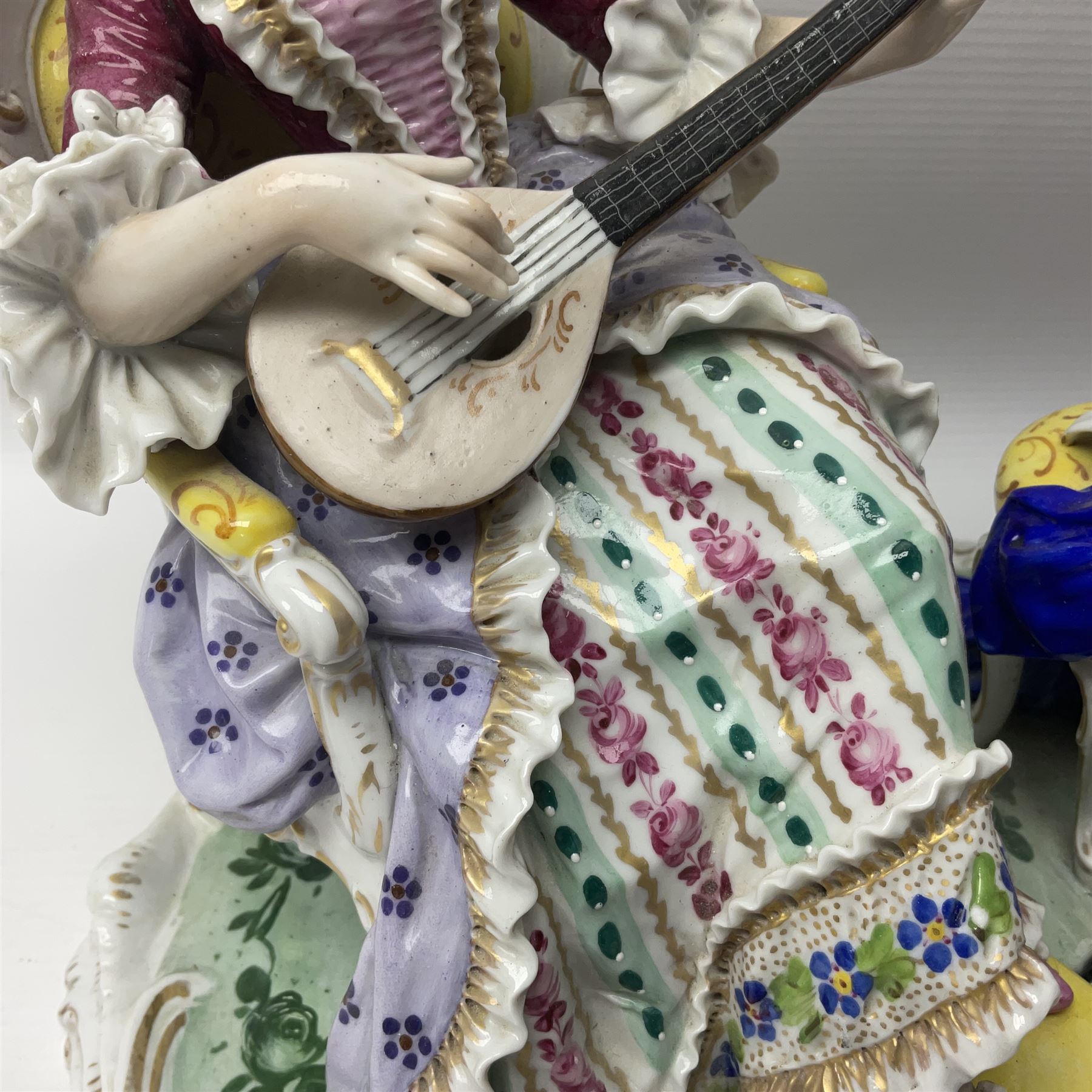 20th century Naples figure group, modelled as a seated female figure playing the lute seated, before a male figure stood holding a sheet of music, each in period dress, upon an oval base with gilt heightened scroll edge, with crowned N mark beneath, H31.5cm L33cm
