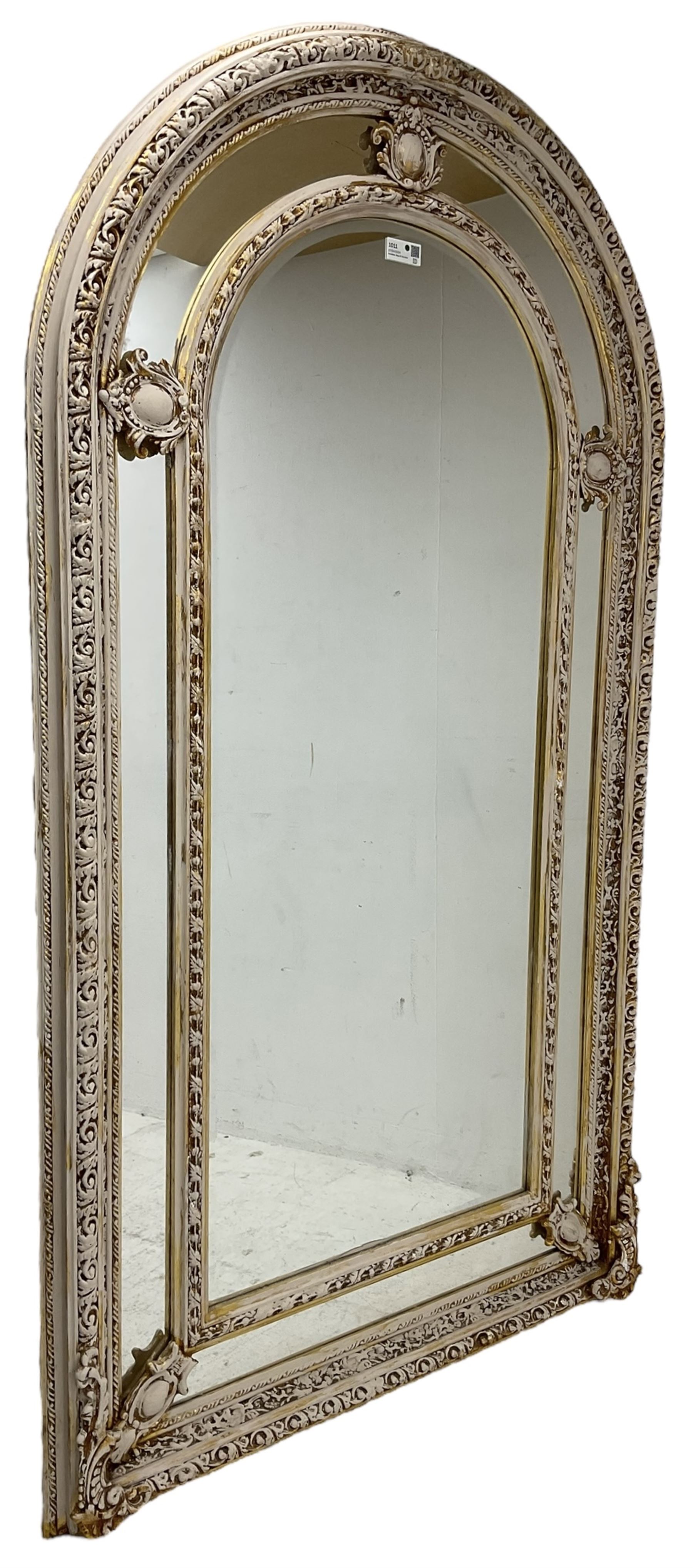 Large painted and gilt arched wall mirror, the frame decorated with scrolling leafy branches, central bevelled mirror mirror surrounded by plain panels, decorated with cartouche mounts 
